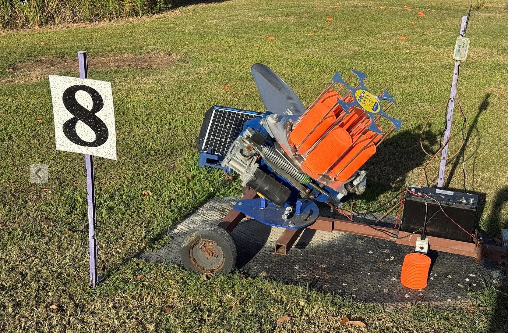 A grass field with a solar powered trap, connected to a battery at a gun club.