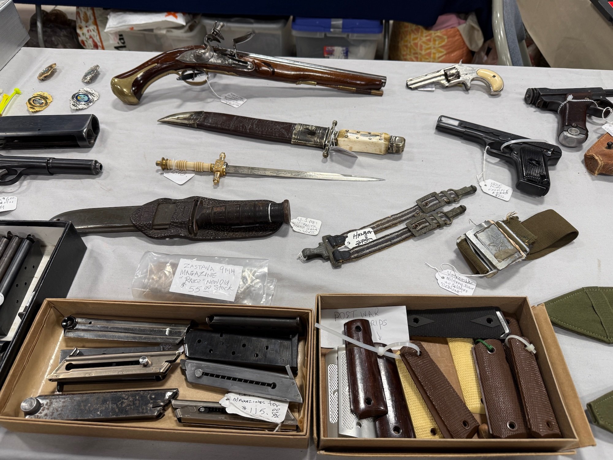 Collection of vintage and toy guns, knives, and knife cases displayed on a table at a gun show.