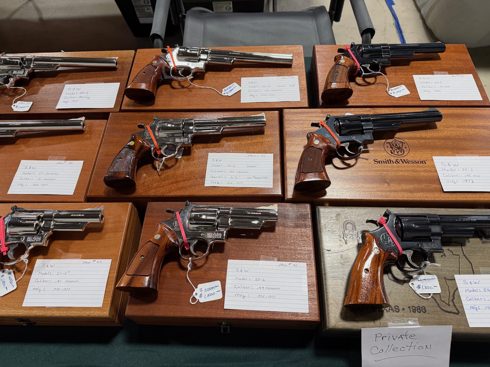 Collection of various Smith & Wesson revolvers displayed on wooden cases with handwritten labels indicating models, calibers, and manufacturing dates, including some with price tags.