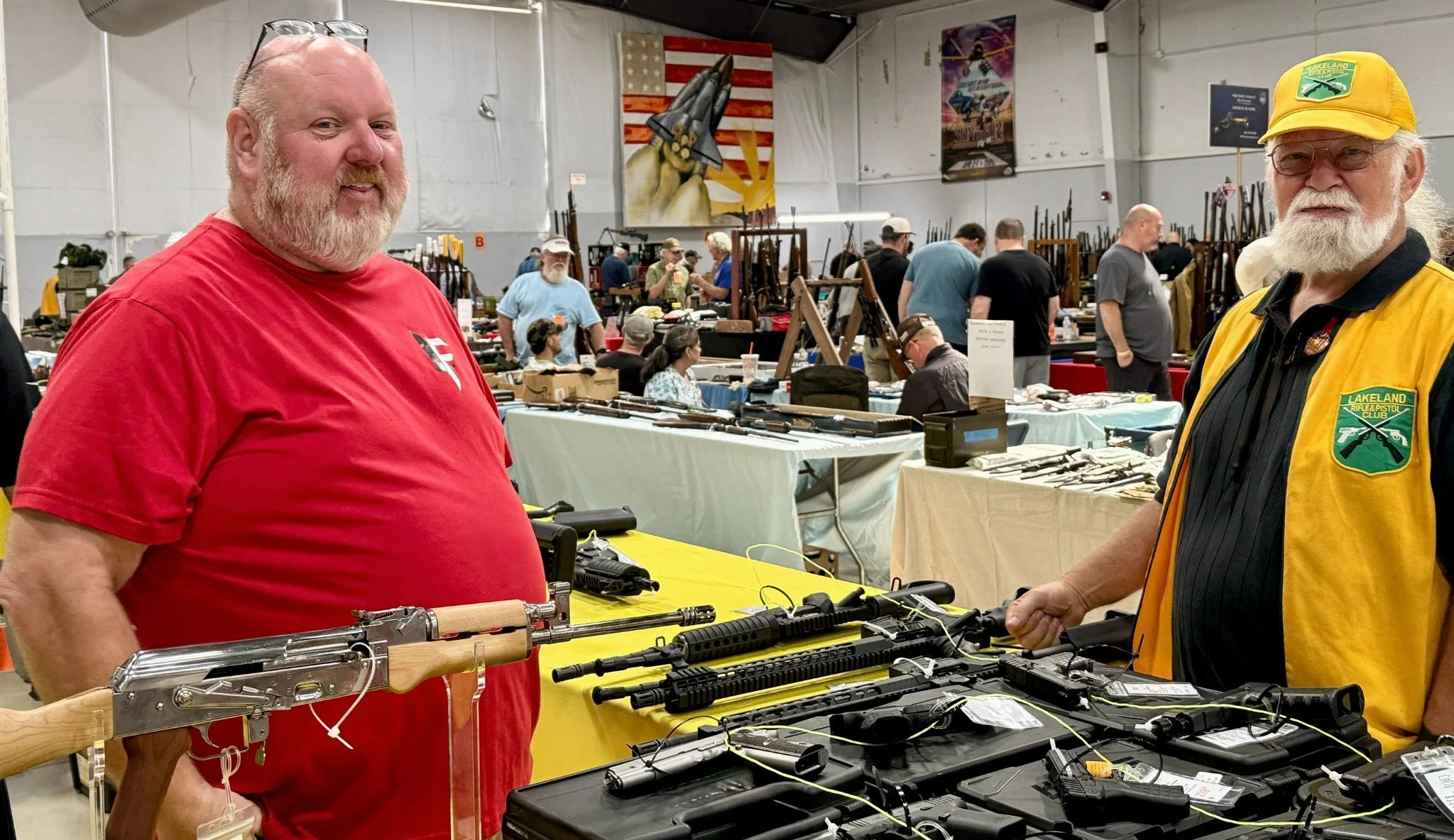 Vendor, Volunteer, and guns on a table; other attendees, vendors, and displays in the background