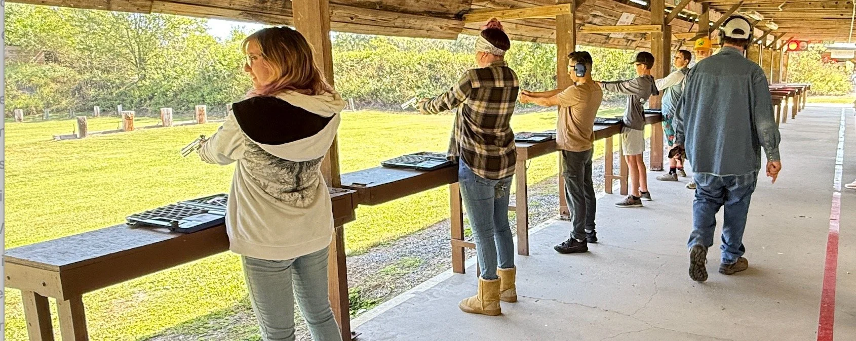 People participating in a shooting range practicing with firearms under a covered outdoor area.