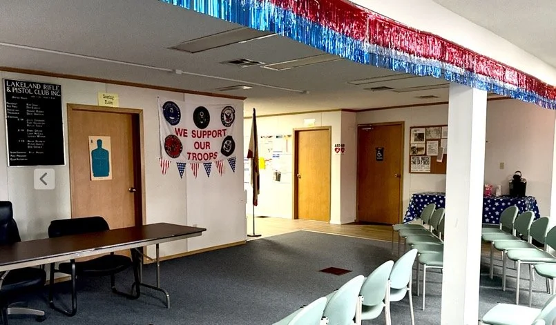 Indoor room decorated with patriotic red, white, and blue decorations supporting military troops, with chairs set up for an event.