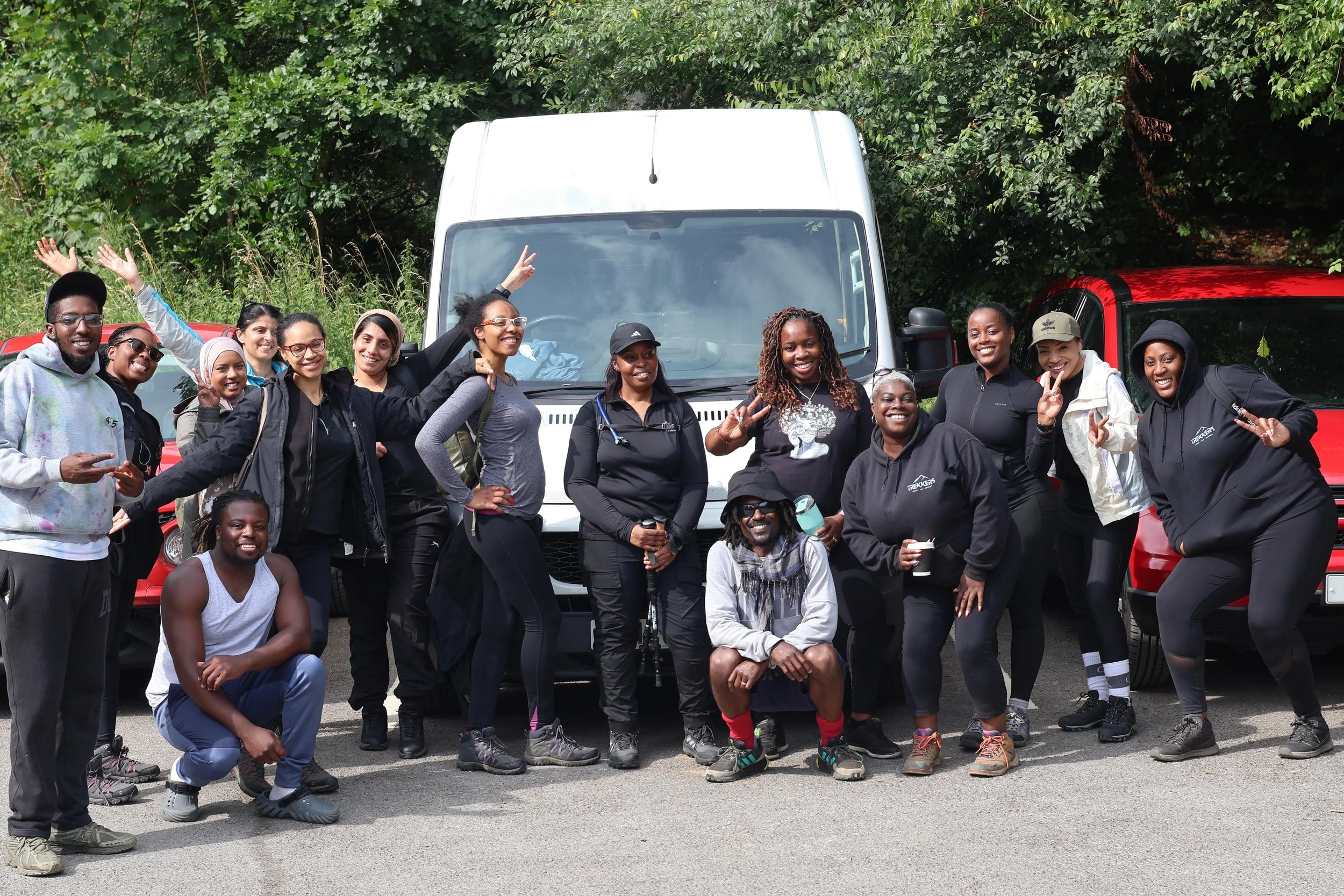 Group of people standing in front of white and red vehicles, smiling and posing outdoors.
