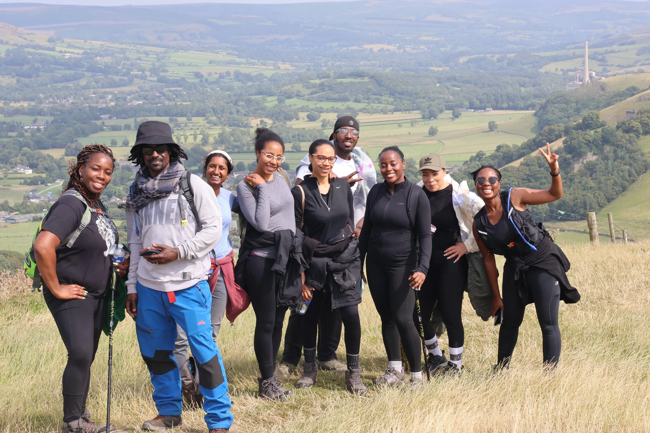 Group of ten diverse people hiking outdoors on a grassy hill, with green fields and rolling hills in the background.