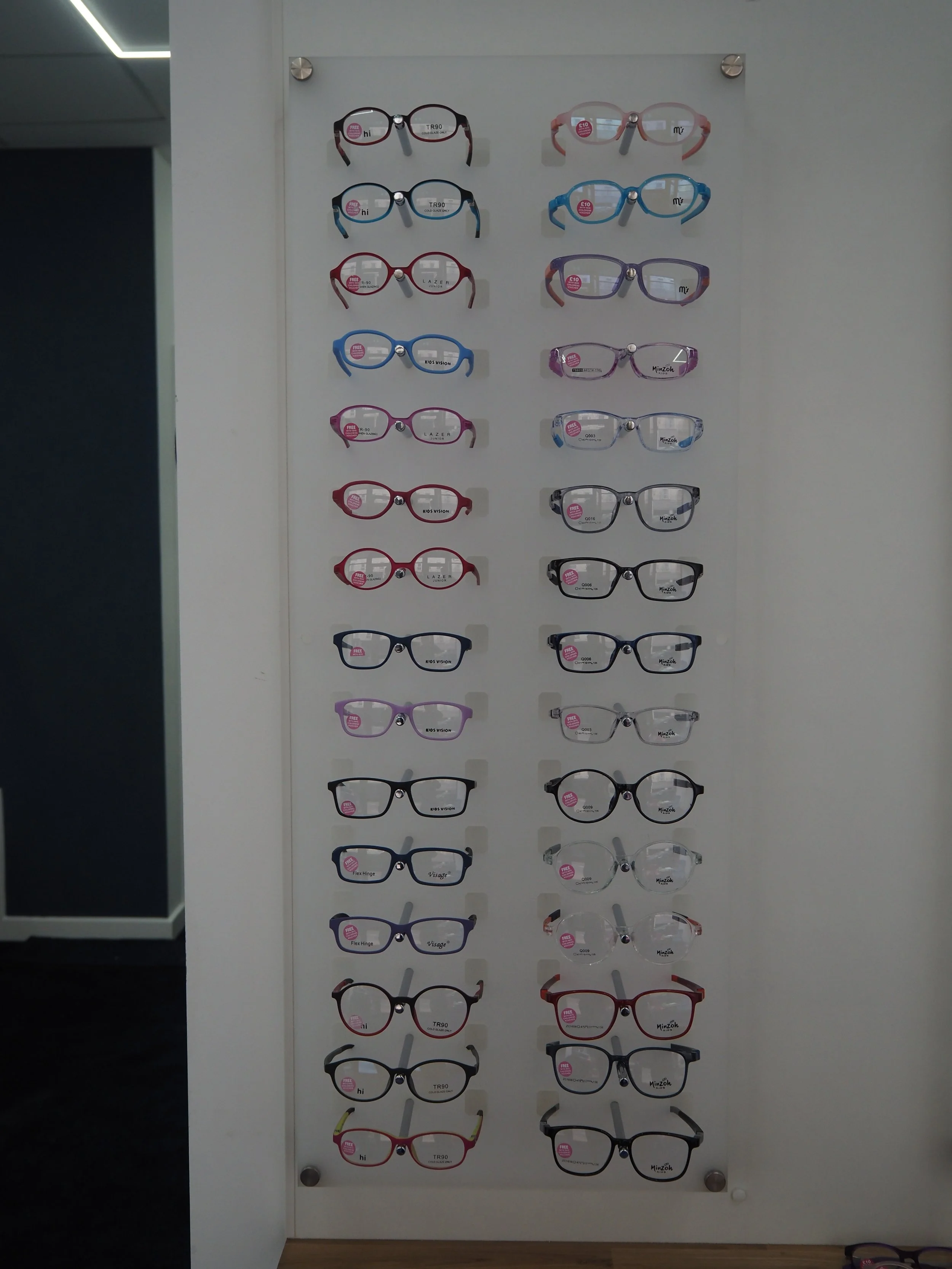 Display of various colorful eyeglasses on a white board inside an optical store.