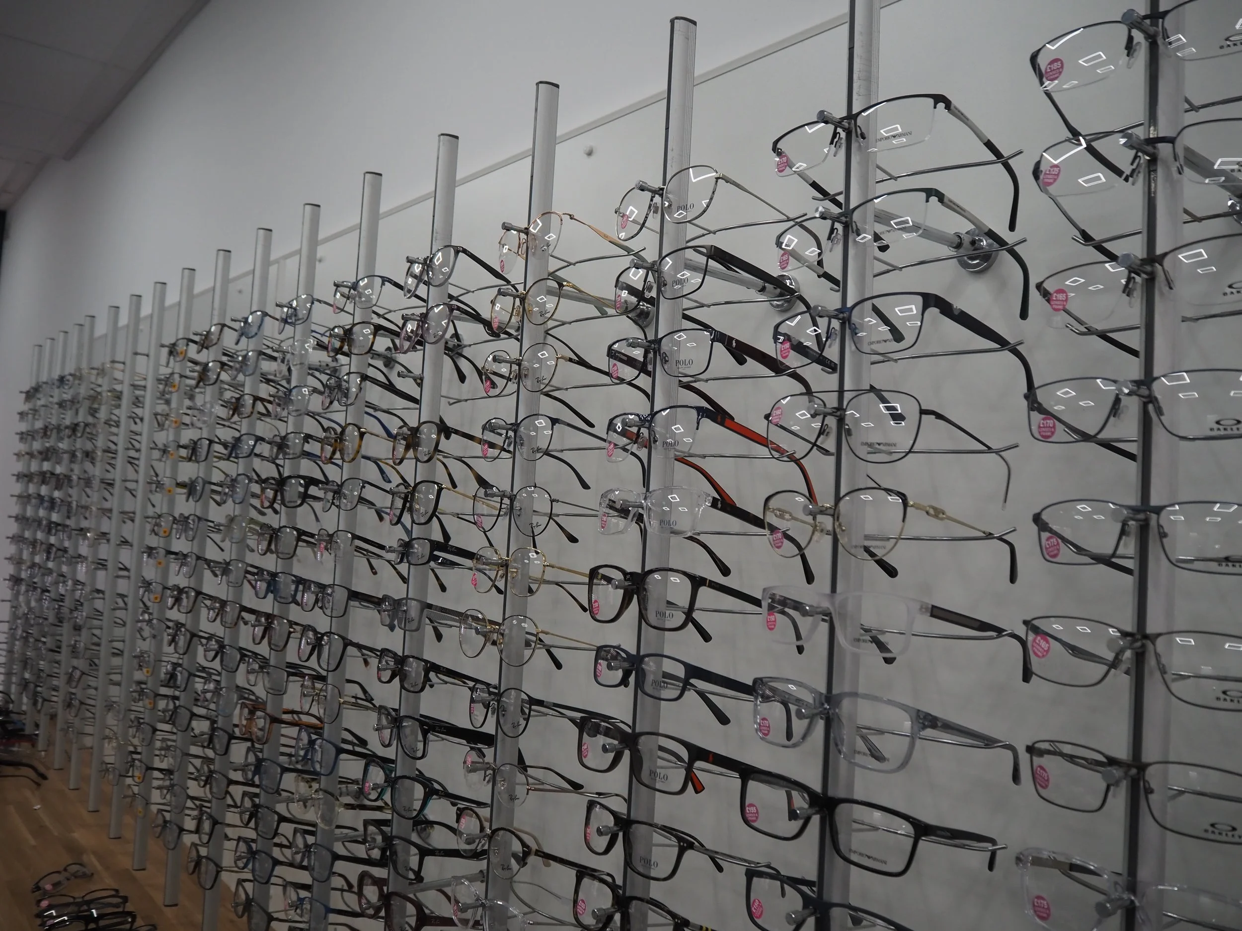 Multiple rows of eyeglasses displayed on vertical display racks at an optical store.