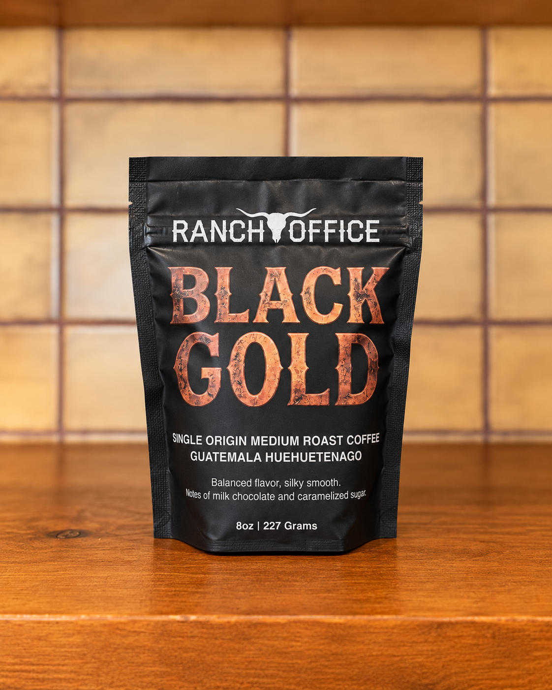 A black package of Ranch Office Black Gold single origin medium roast coffee from Guatemala, placed on a wooden surface in front of a tiled wall.