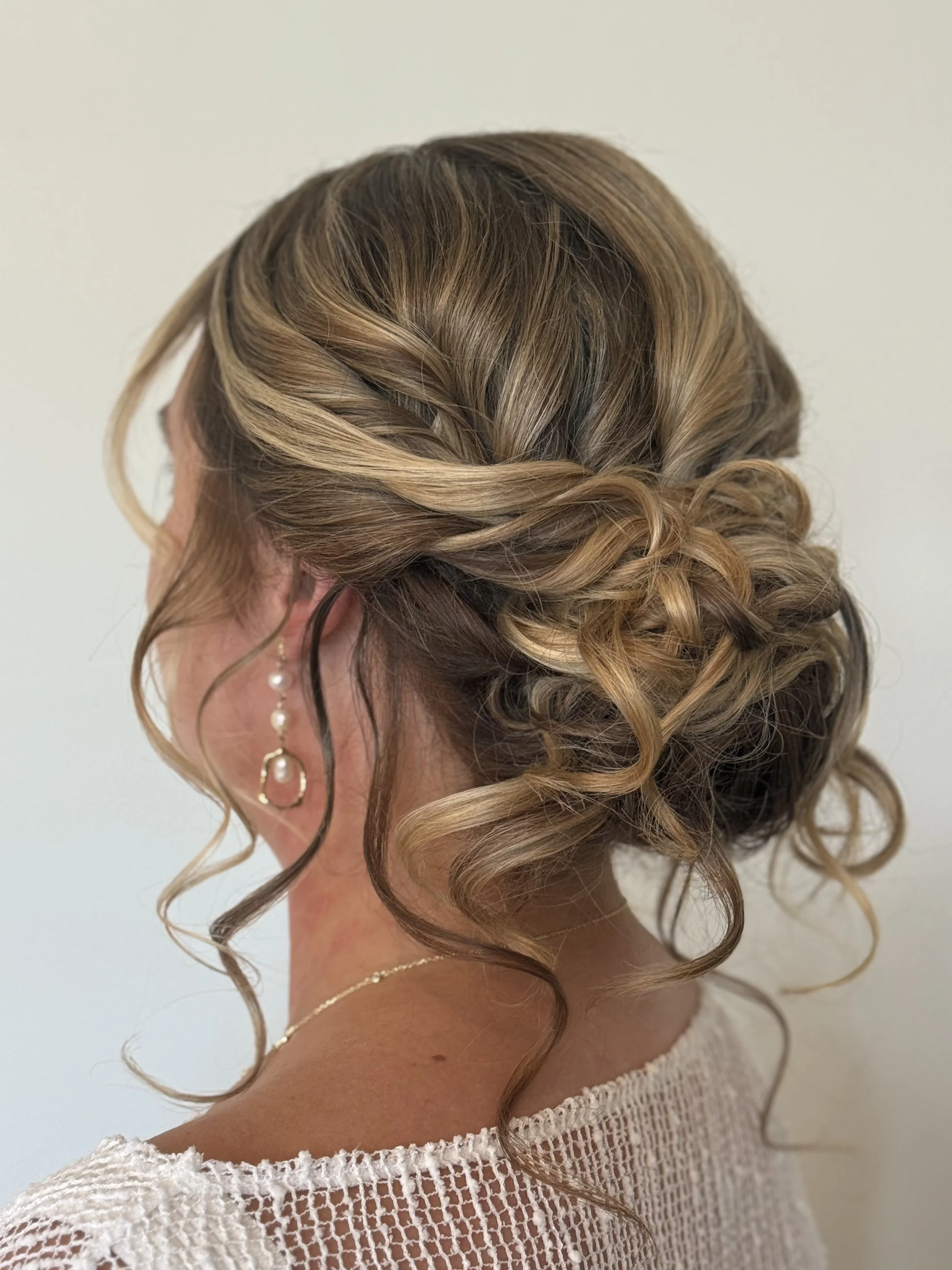 Side view of romantic wedding updo styled by Betsy against a neutral background