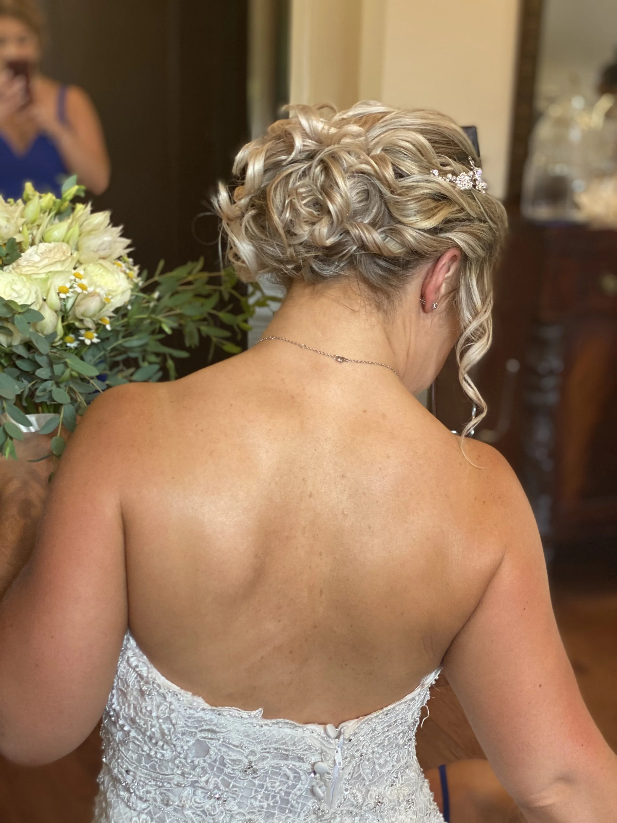 Back view of a bride's romantic wedding updo by Modern Designs stylist Betsy. Bride is wearing a strapless white dress.