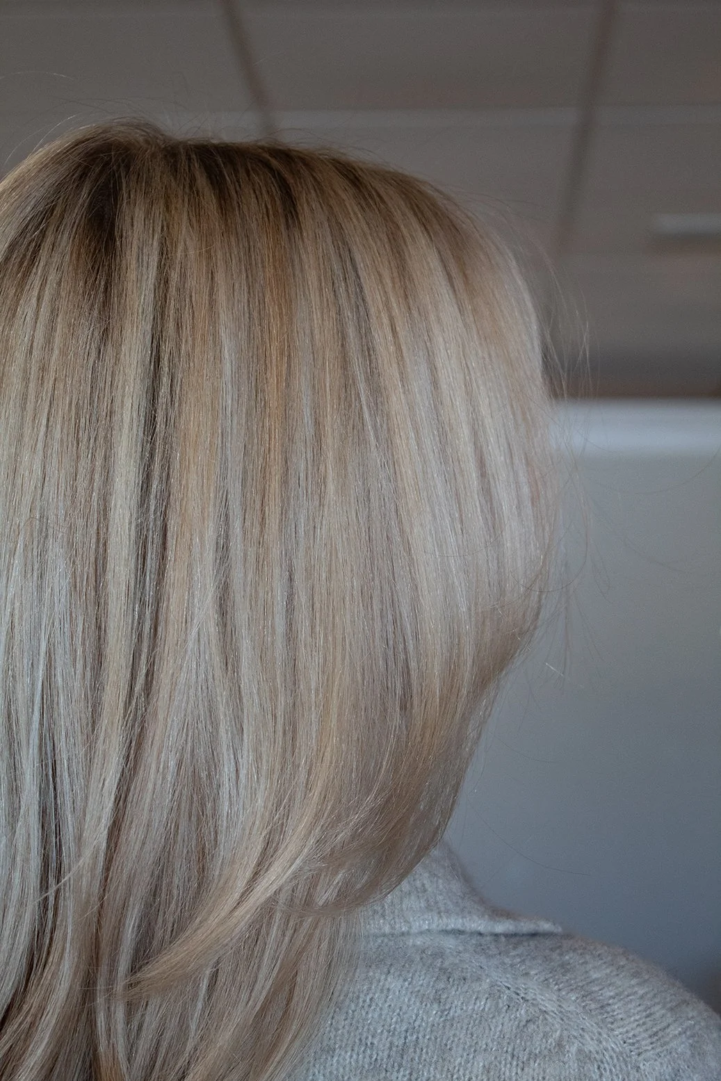 Close-up side-view photo of a client with blonde highlights that cover her face against a blurred salon backdrop.