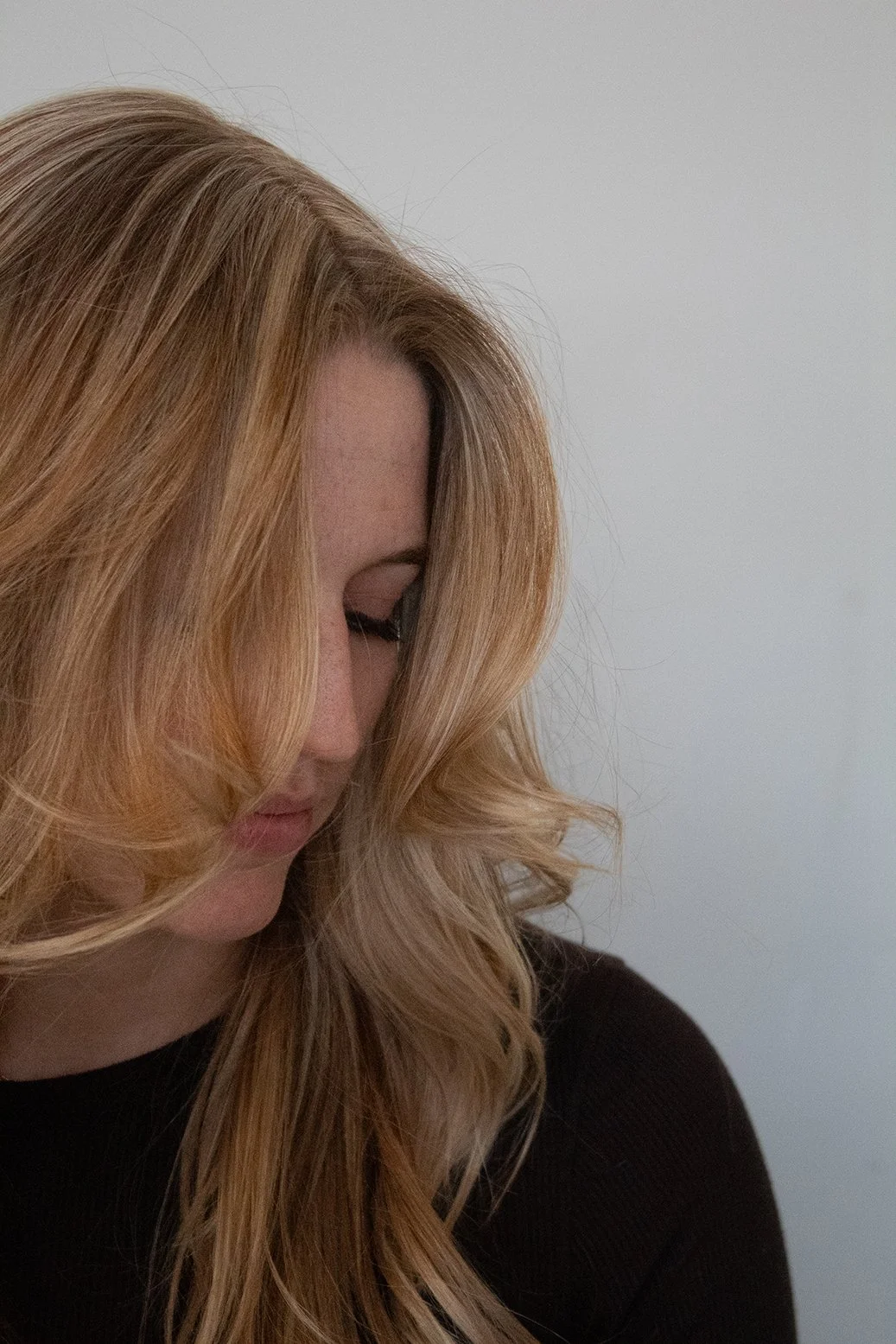 Side view of a client with strawberry blonde hair that partially covers her face as she looks downward against a white backdrop.