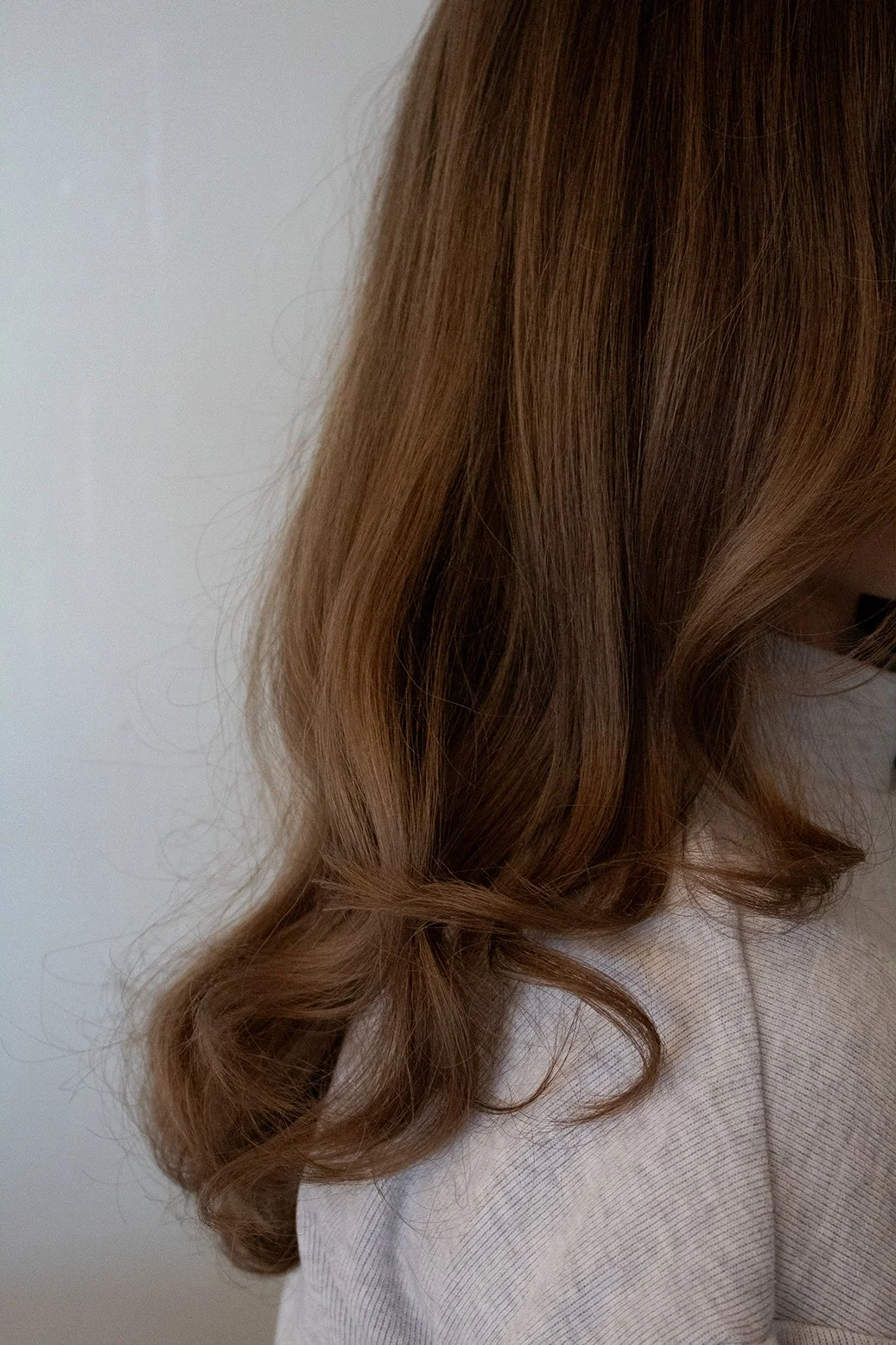 Close-up of a client's brunette hair, styled with curls against a white backdrop.