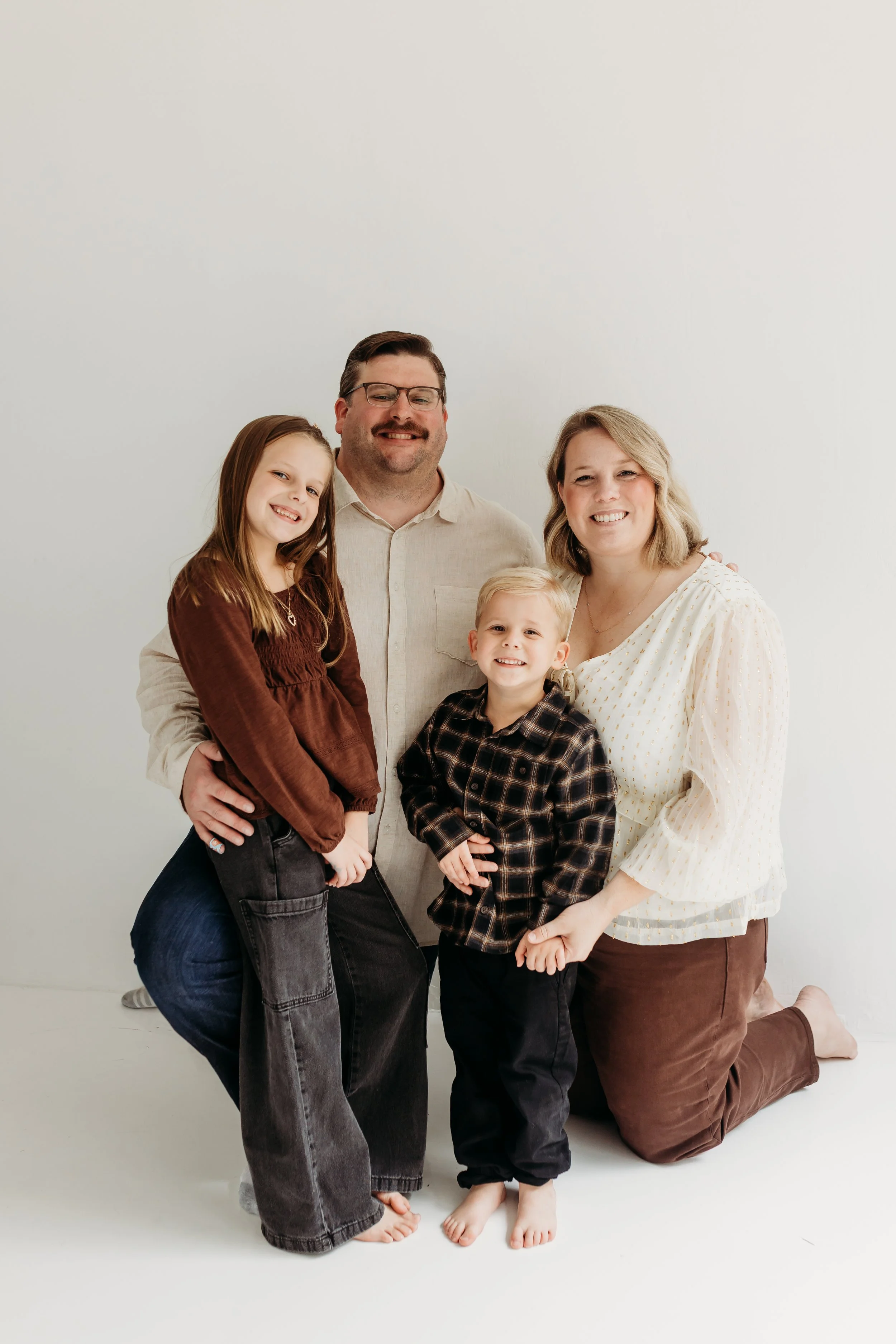 A family of five posing together against a plain white background, smiling and dressed in casual clothing.