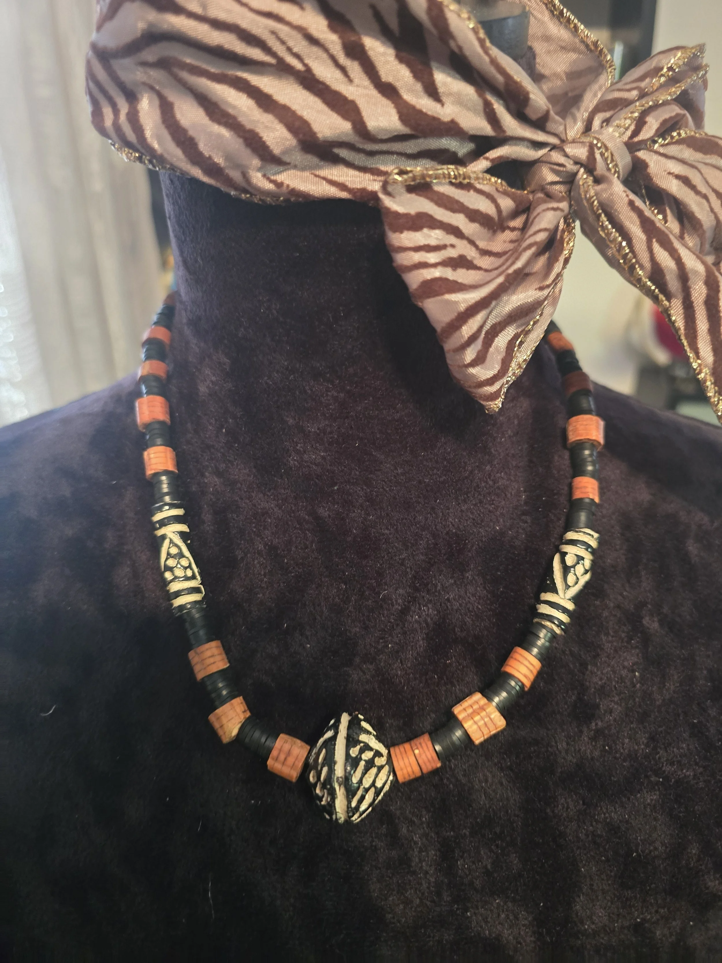 Black and beige beaded necklace with tribal patterns on a mannequin with a purple velvet top and a zebra-print silk scarf tied in a bow around the neck.