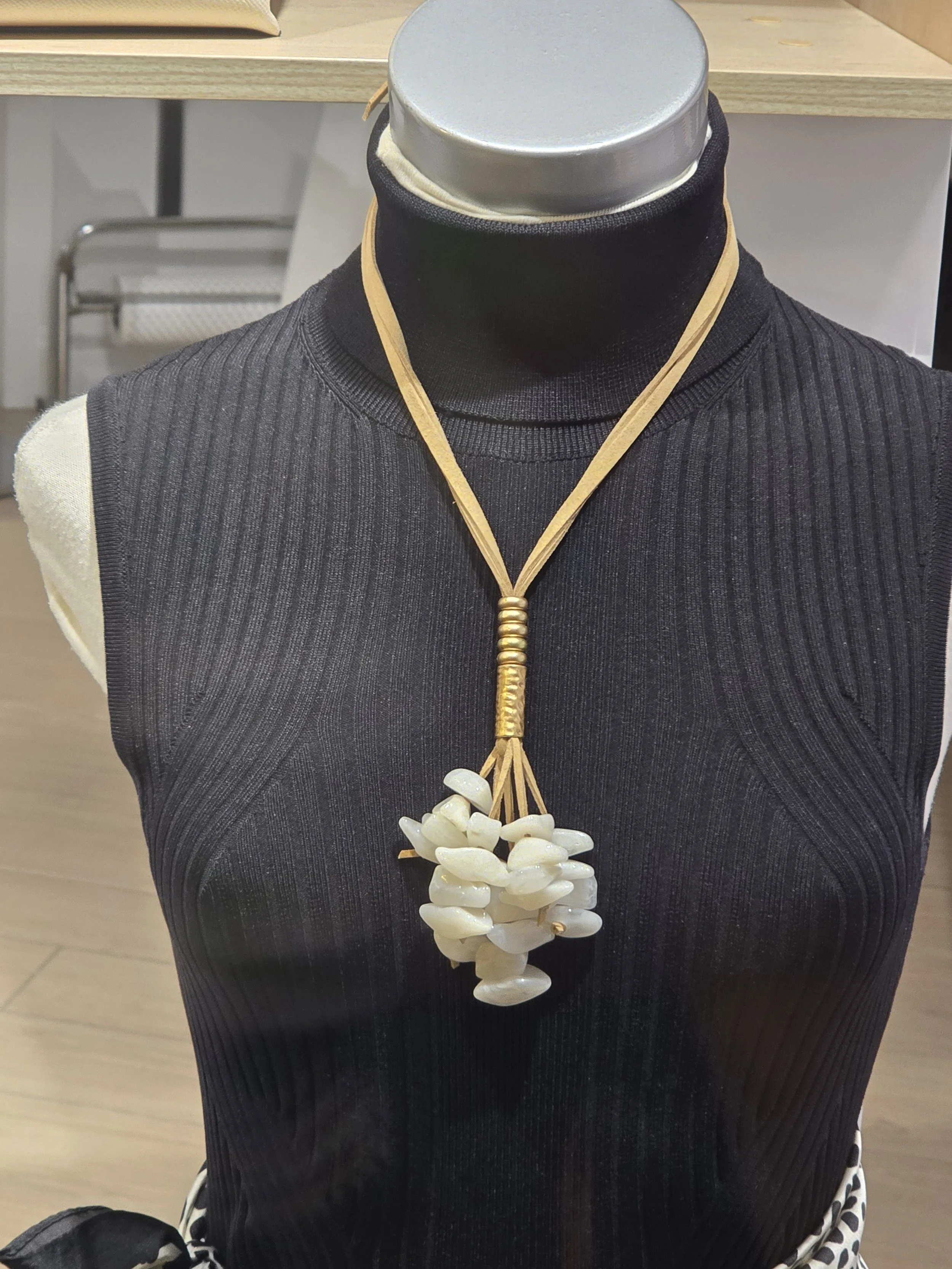 Mannequin dressed in a black ribbed sleeveless top with a shell necklace.