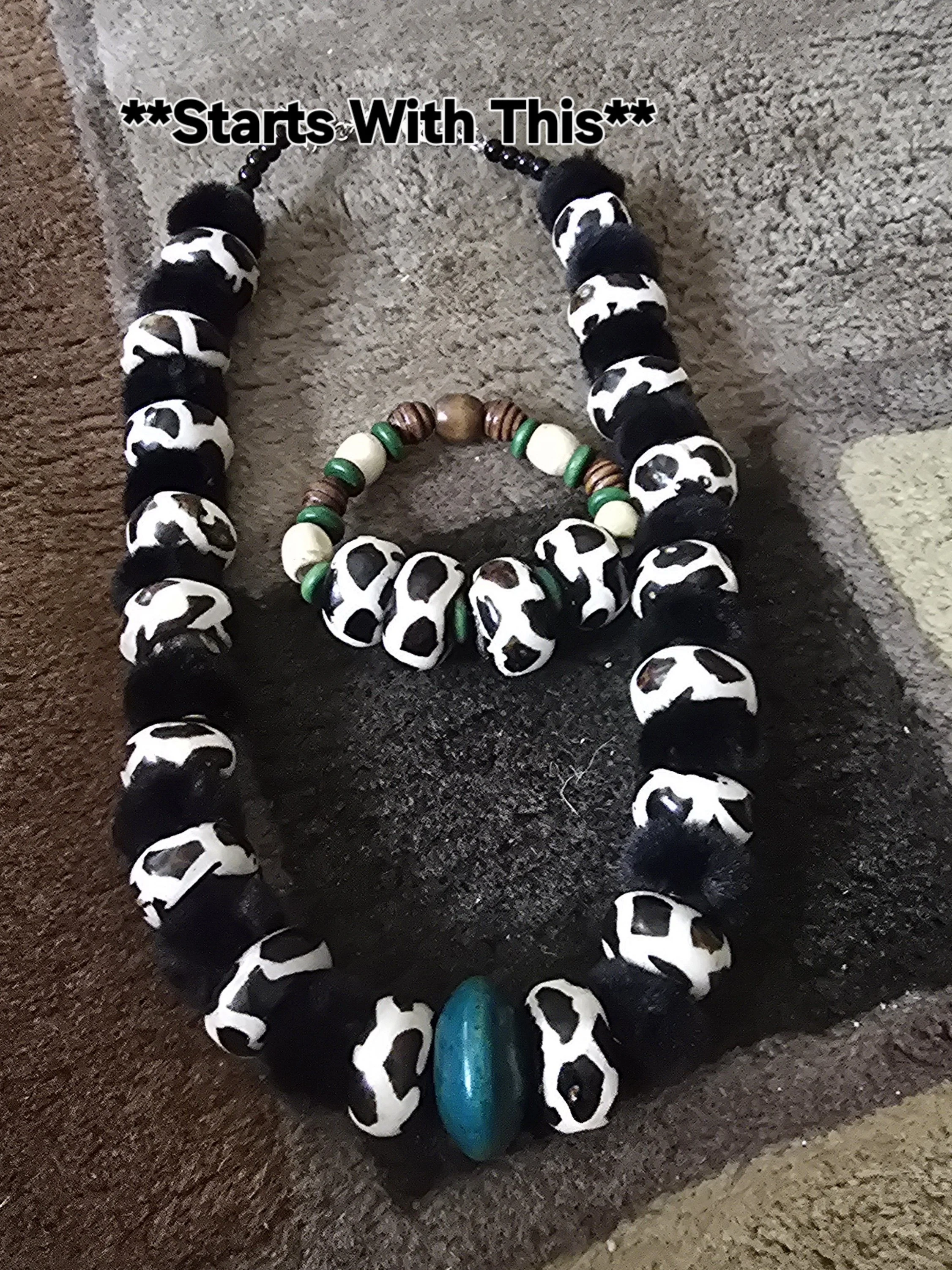 Three beaded necklaces of different sizes and colors, with the largest necklace featuring black and white cow print beads, a large turquoise bead at the bottom, and the text '**Starts With This**' above it.