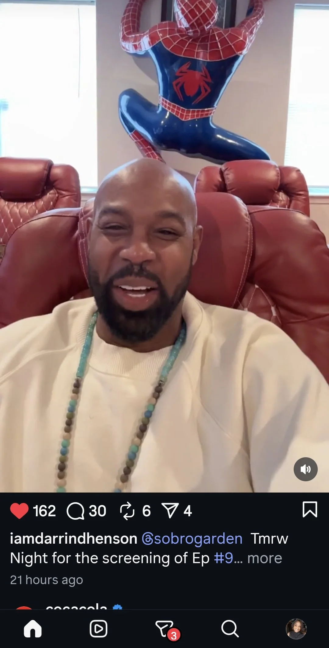 Darrin Henson wearing a necklace sitting on a red leather chair, smiling. Behind him, a Spider-Man balloon is placed on the wall.