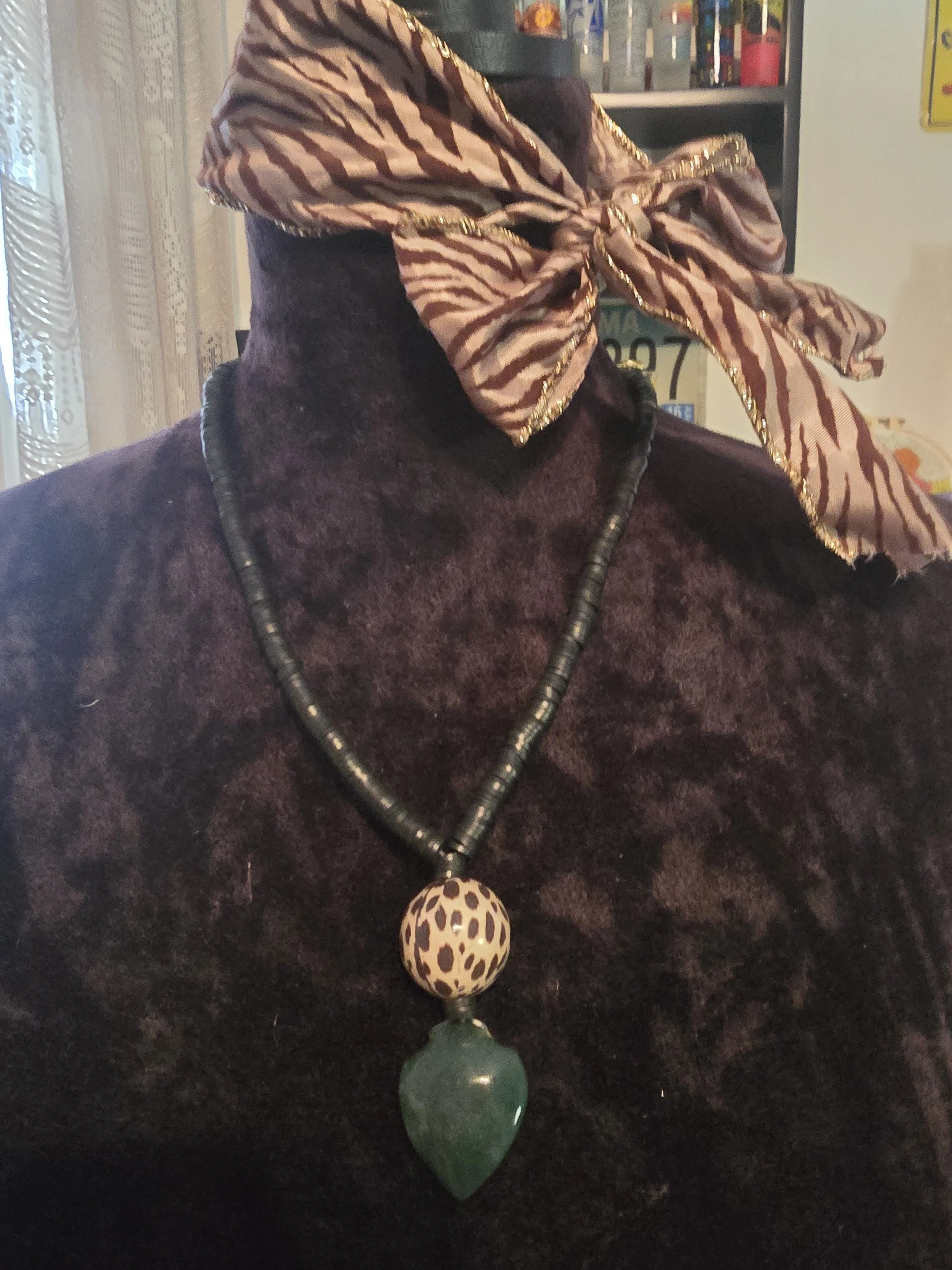 Close-up of a mannequin wearing a black velvet top, a large animal print scarf with gold trim tied around the head, and a beaded necklace with large leopard-print and green leaf-shaped pendants.