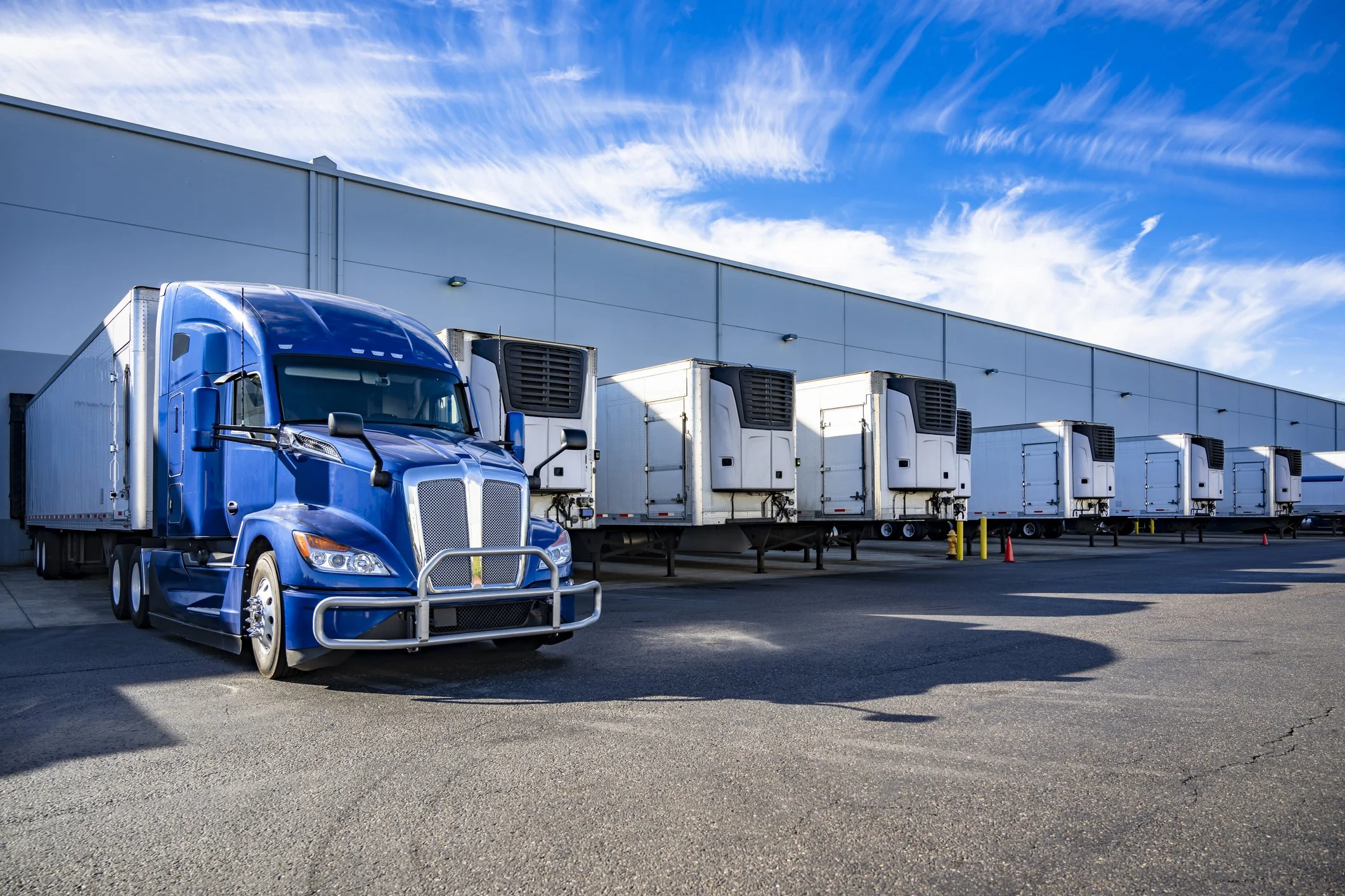 A row of refrigerated trucks parked outside a warehouse on a sunny day.