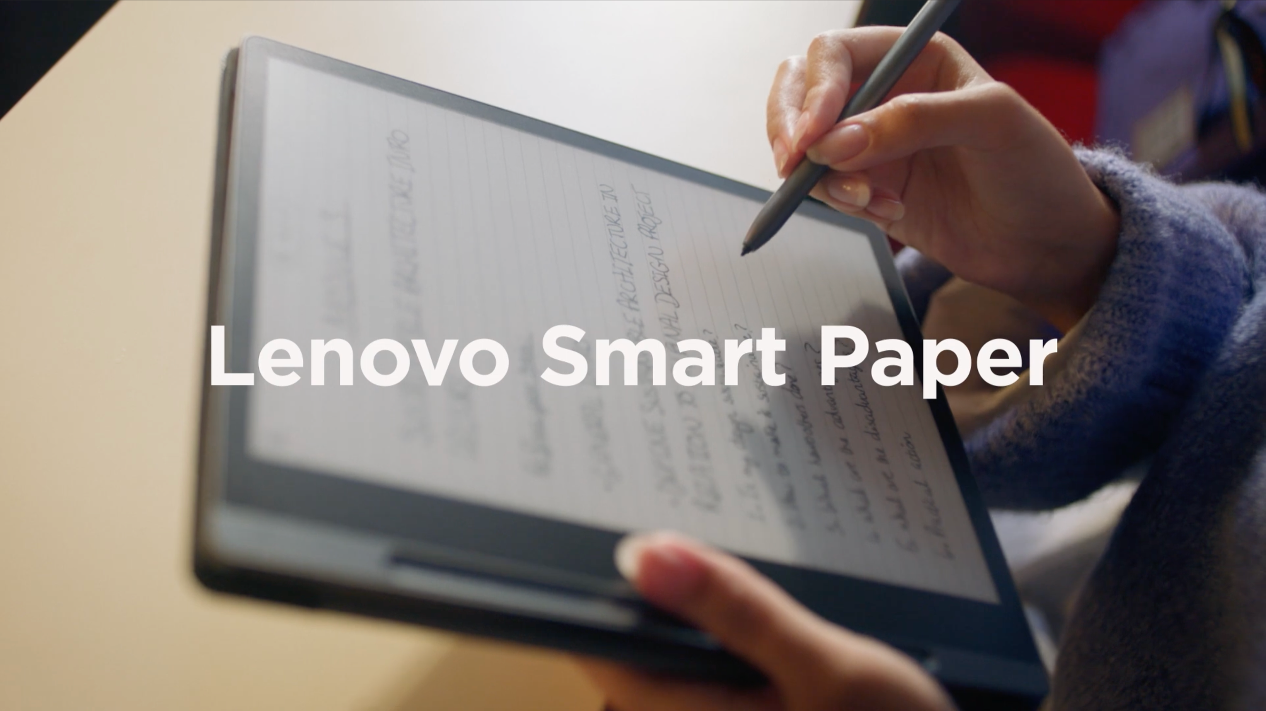 Close-up of a person holding a Lenovo Smart Paper e-ink tablet and writing on it with a stylus, with handwritten notes visible.