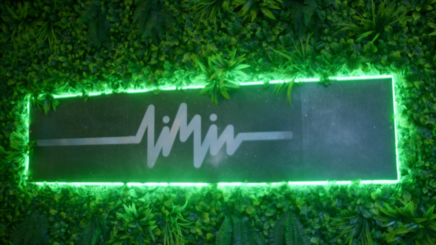 Neon sign with a heartbeat line and stylized letters, surrounded by green foliage and illuminated green.