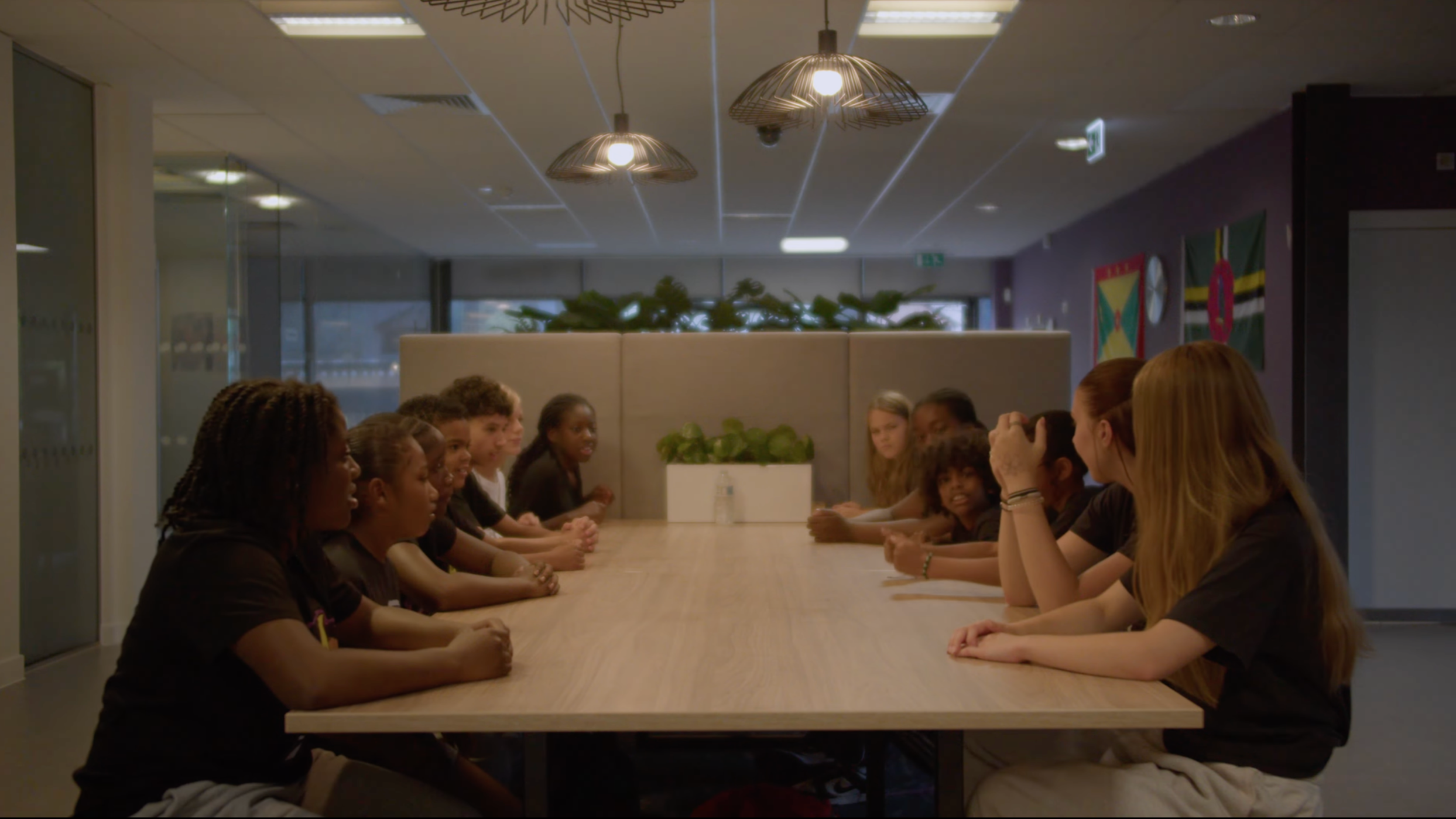 Group of diverse young women sitting at a long conference table in a modern office or meeting room.
