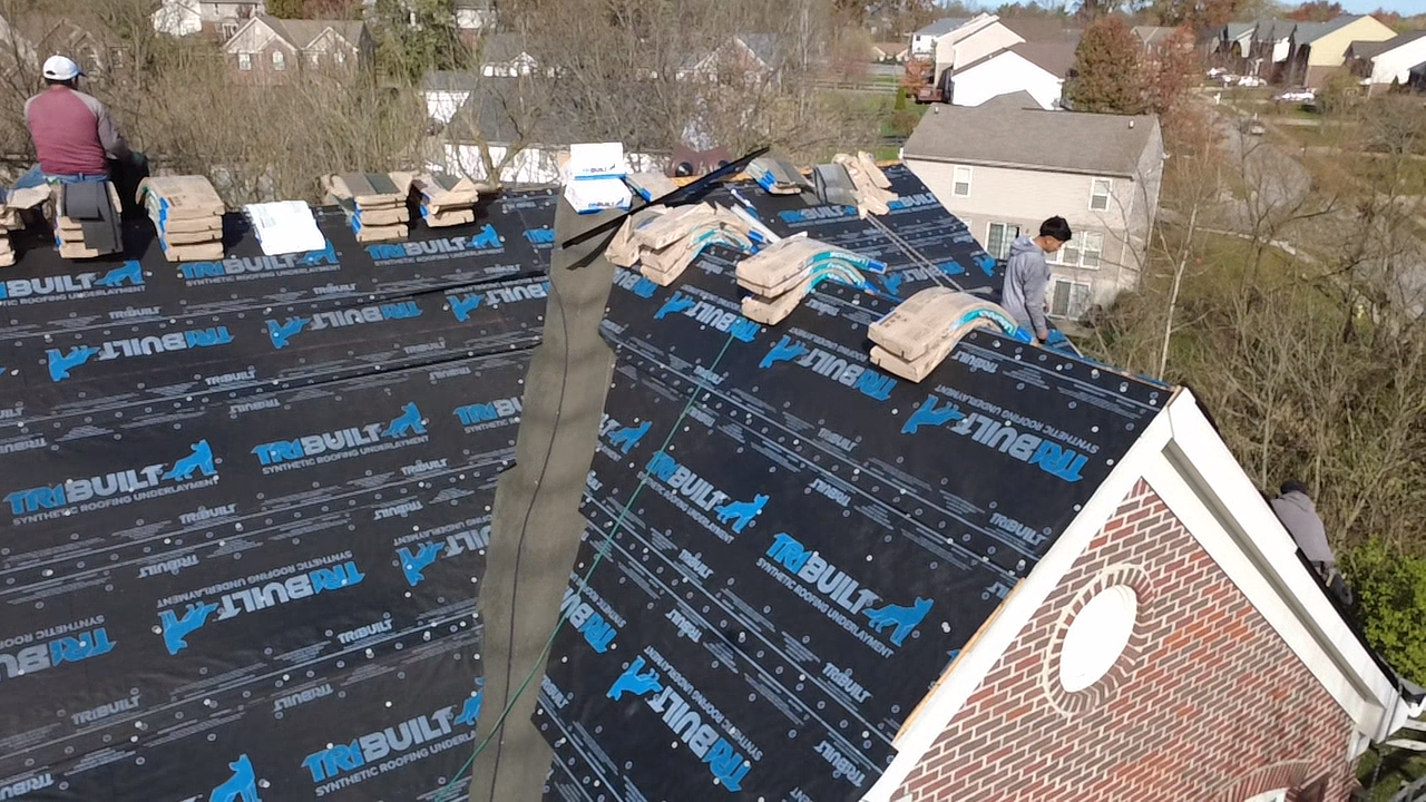 View of a house roof under construction with workers installing synthetic roofing underlayment branded 'TRIBUILT'. Roof Replacement in Union KY – Code-Compliant & CertainTeed Certified