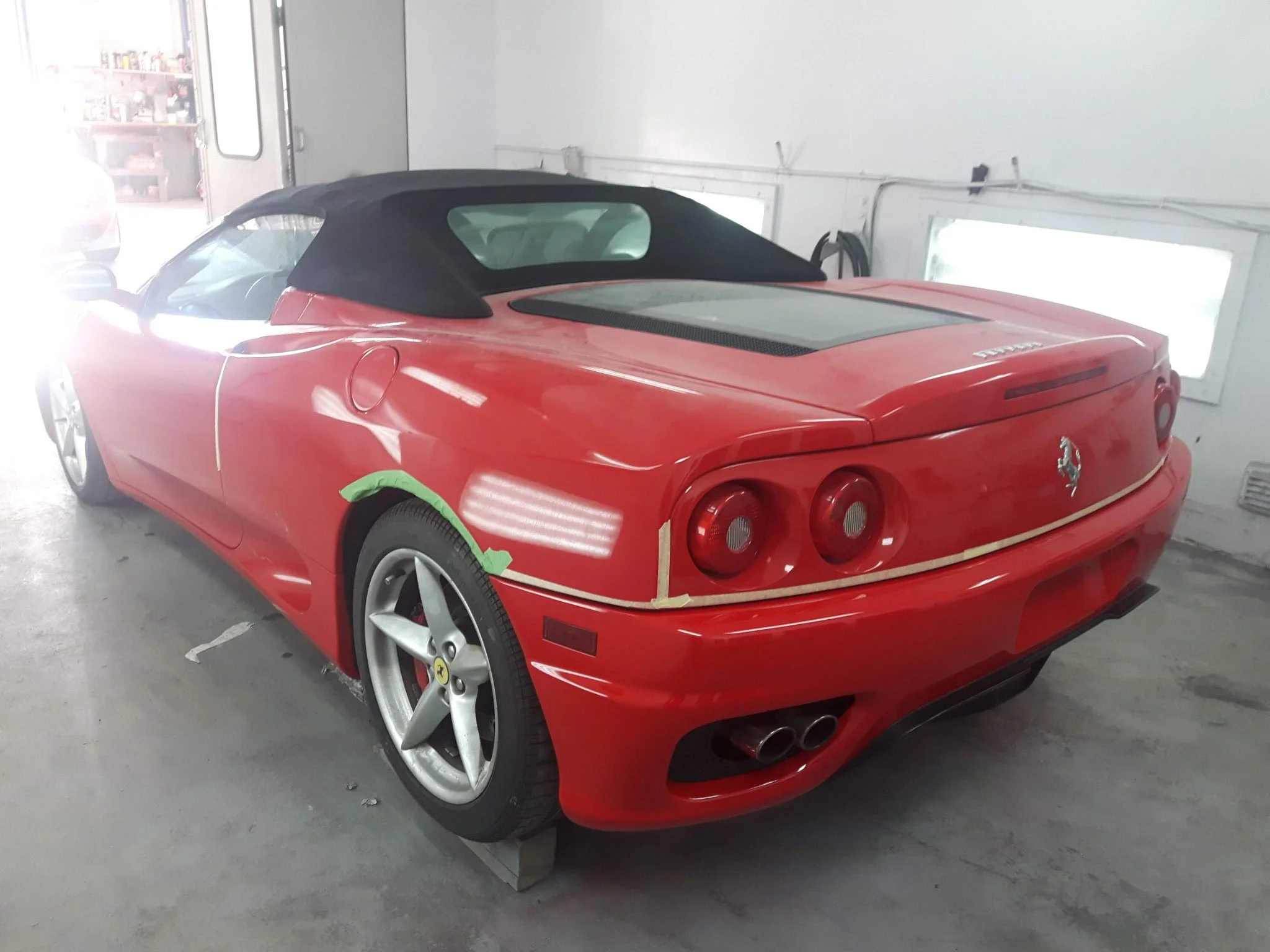 Red Ferrari sports car with a black convertible top inside a garage, with masking tape on the side panel.
