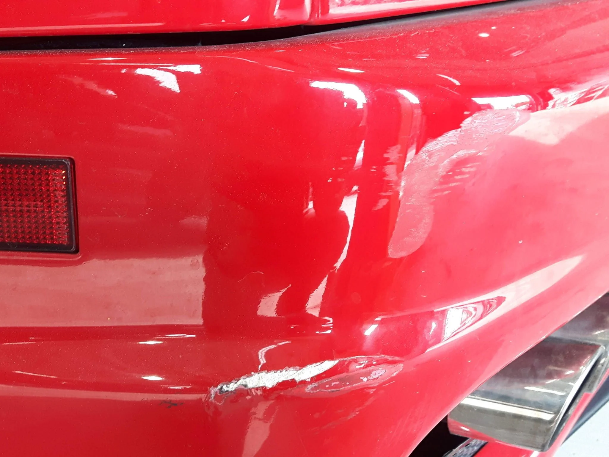 Close-up photo of a red vehicle's damaged front panel, showing scratches and a dent.
