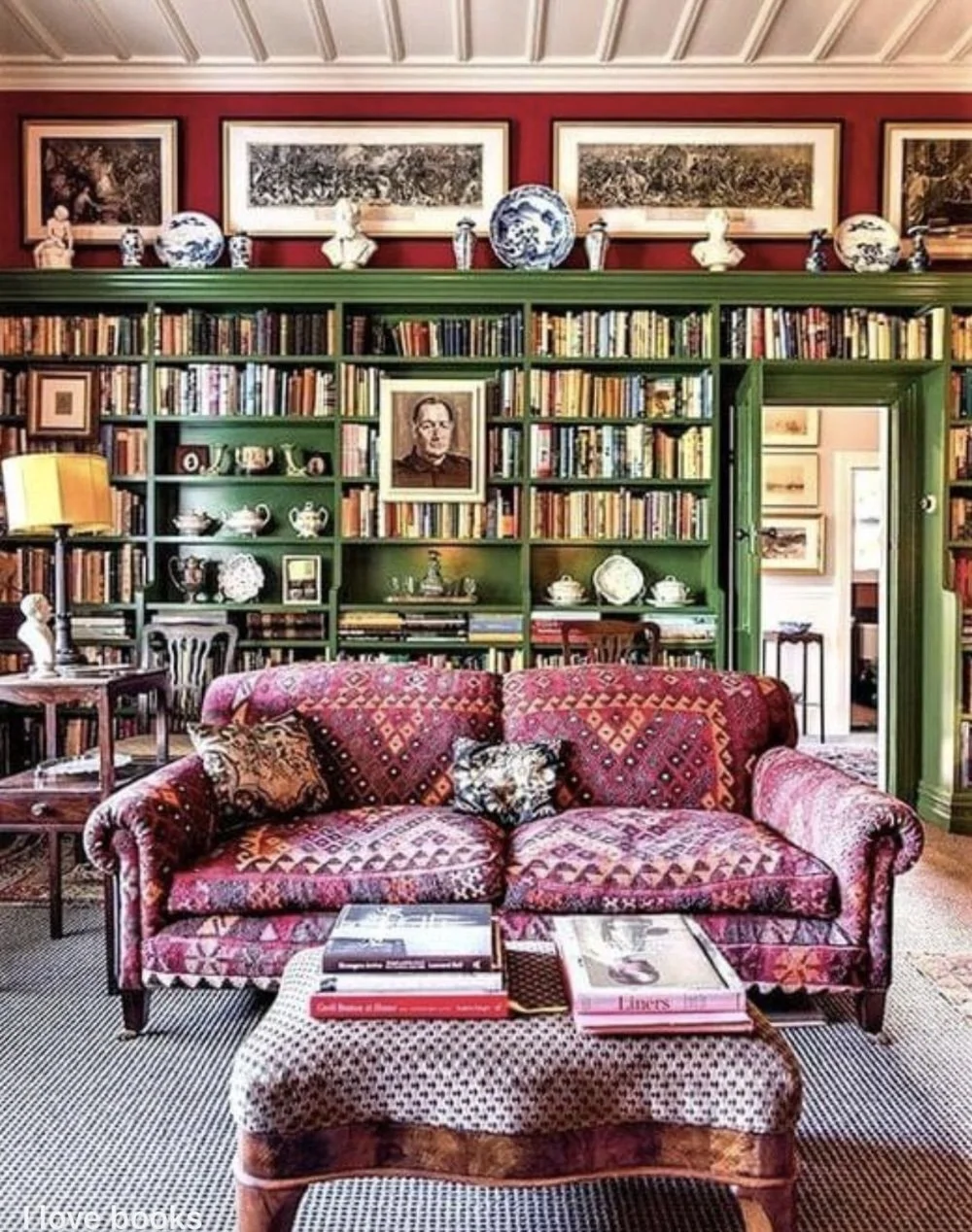 Maximalist library with colorful kilim patterned sofa, emerald green built-in bookshelves, red walls, and blue and white porcelain collection, English country style