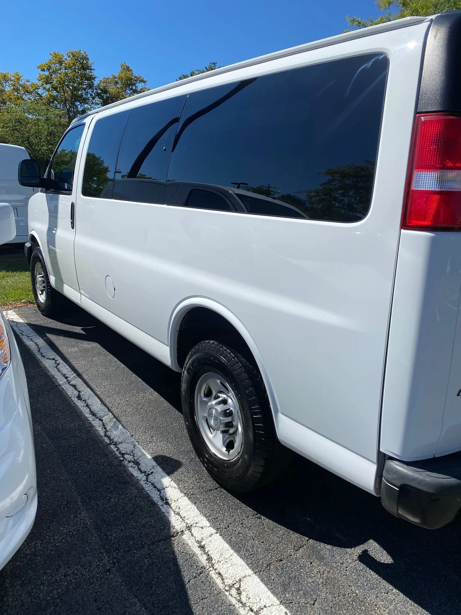 White van parked in a parking lot next to other vehicles, with trees and a clear blue sky in the background.