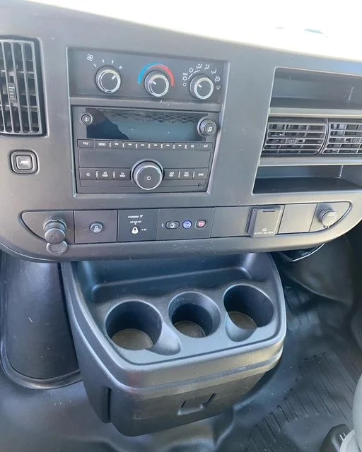 Dashboard of a vehicle showing air conditioning controls, radio, and cup holders.