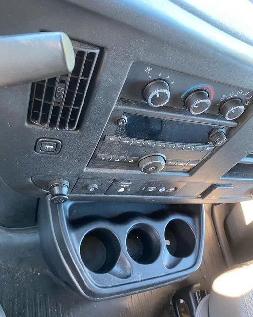 Close-up of car dashboard with air vents, climate control knobs, and a radio, along with a cup holder and part of the steering wheel.