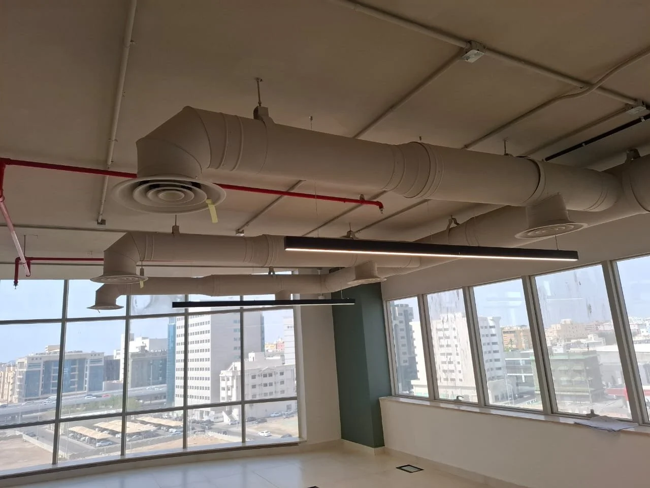 Interior of an office space with large windows, exposed ceiling ducts, and modern linear black light fixtures.