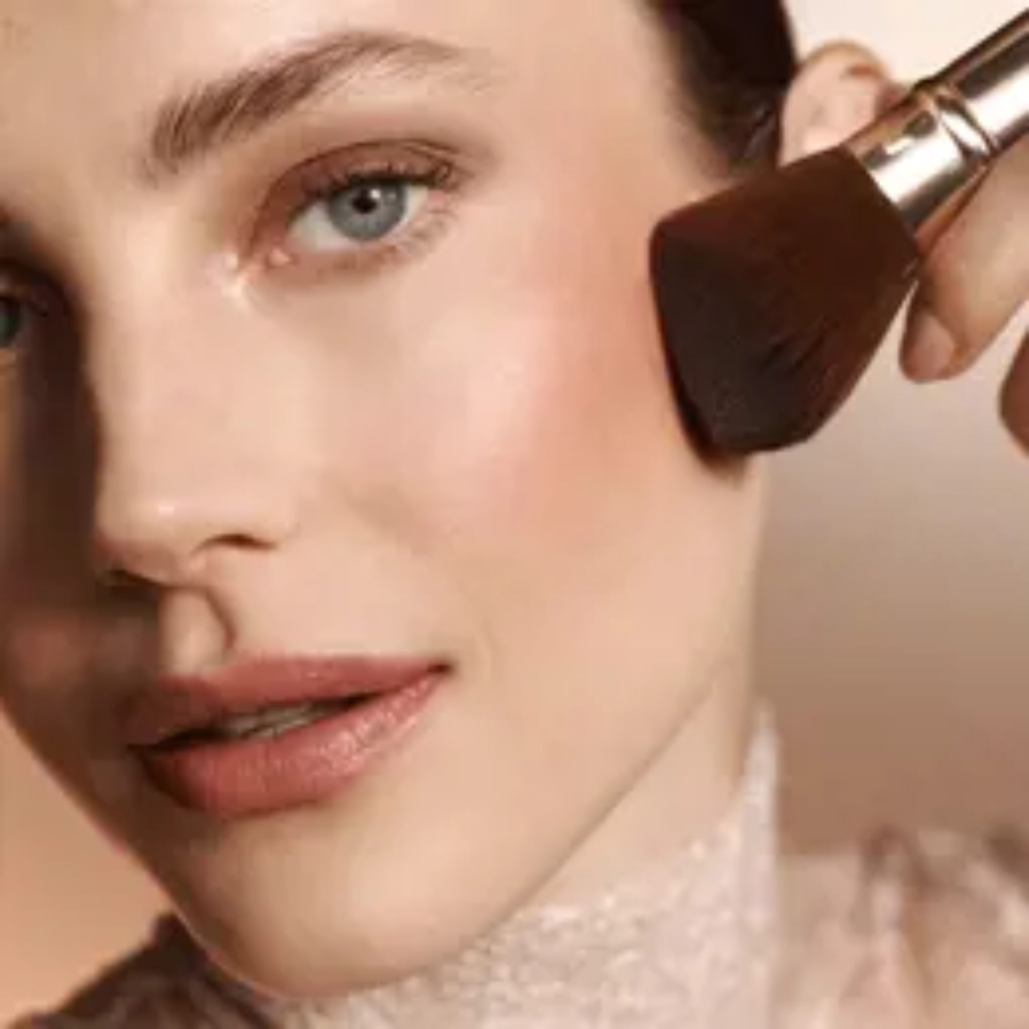 Primer plano de una mujer aplicándose maquillaje con una brocha en el rostro.