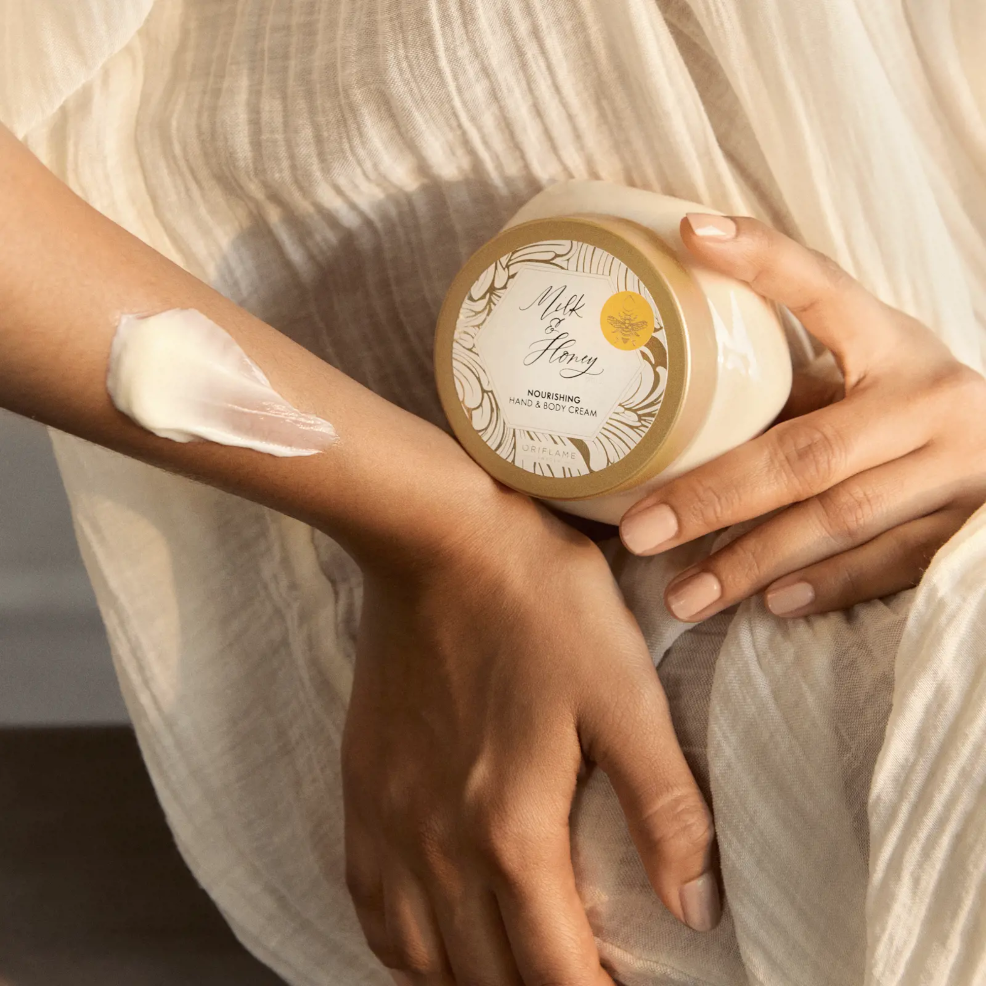 Persona aplicándose la crema Milk & Honey Nourishing Hand & Body Cream de Oriflame en el brazo.