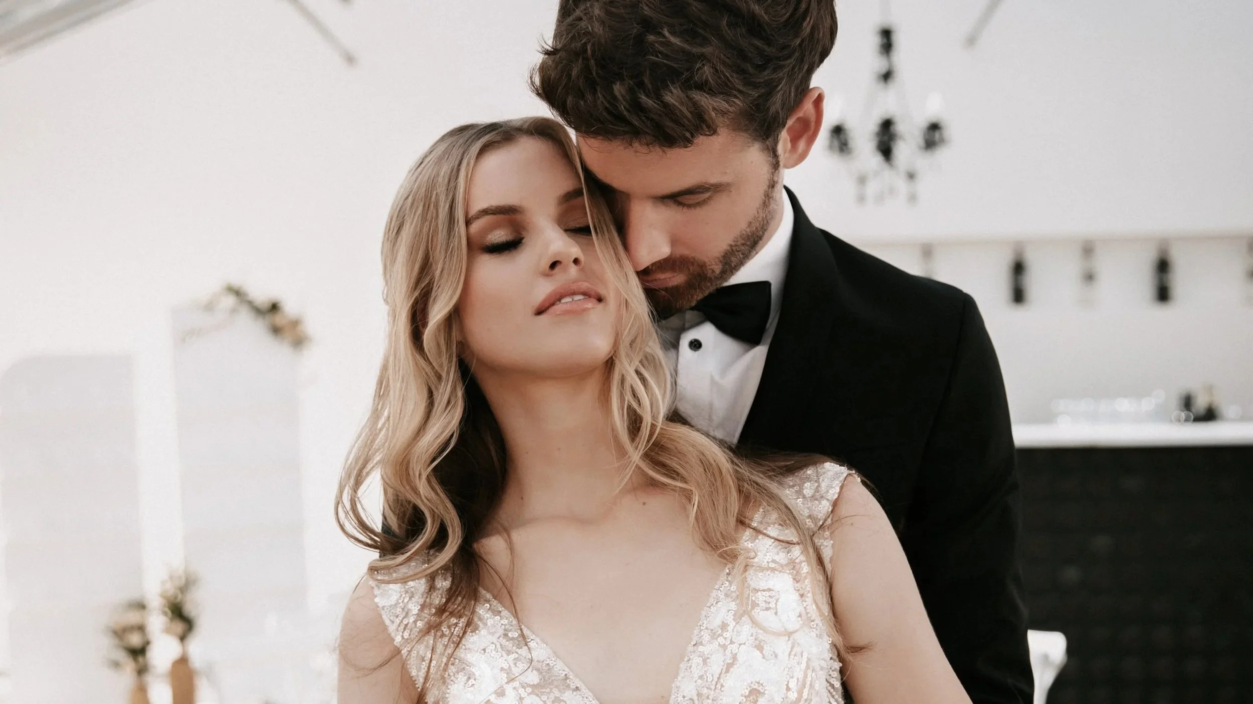 Ein Brautpaar bei einer Hochzeitszeremonie, die Braut trägt ein weißes Kleid mit Spitzen und der Bräutigam einen schwarzen Anzug mit Fliege.