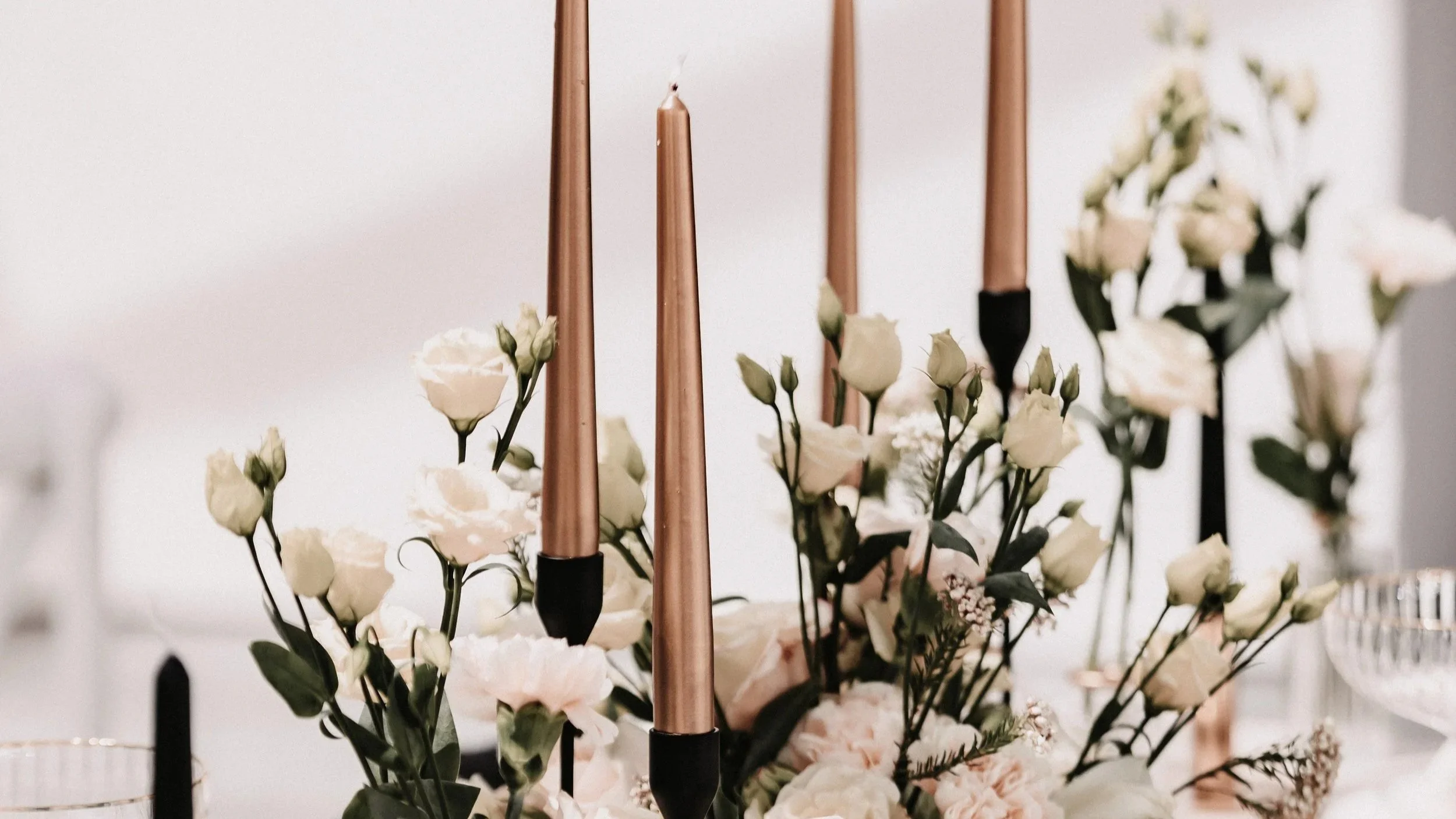 Kerzenständer mit weißen Blumen und grünen Blättern auf einem festlich gedeckten Tisch.