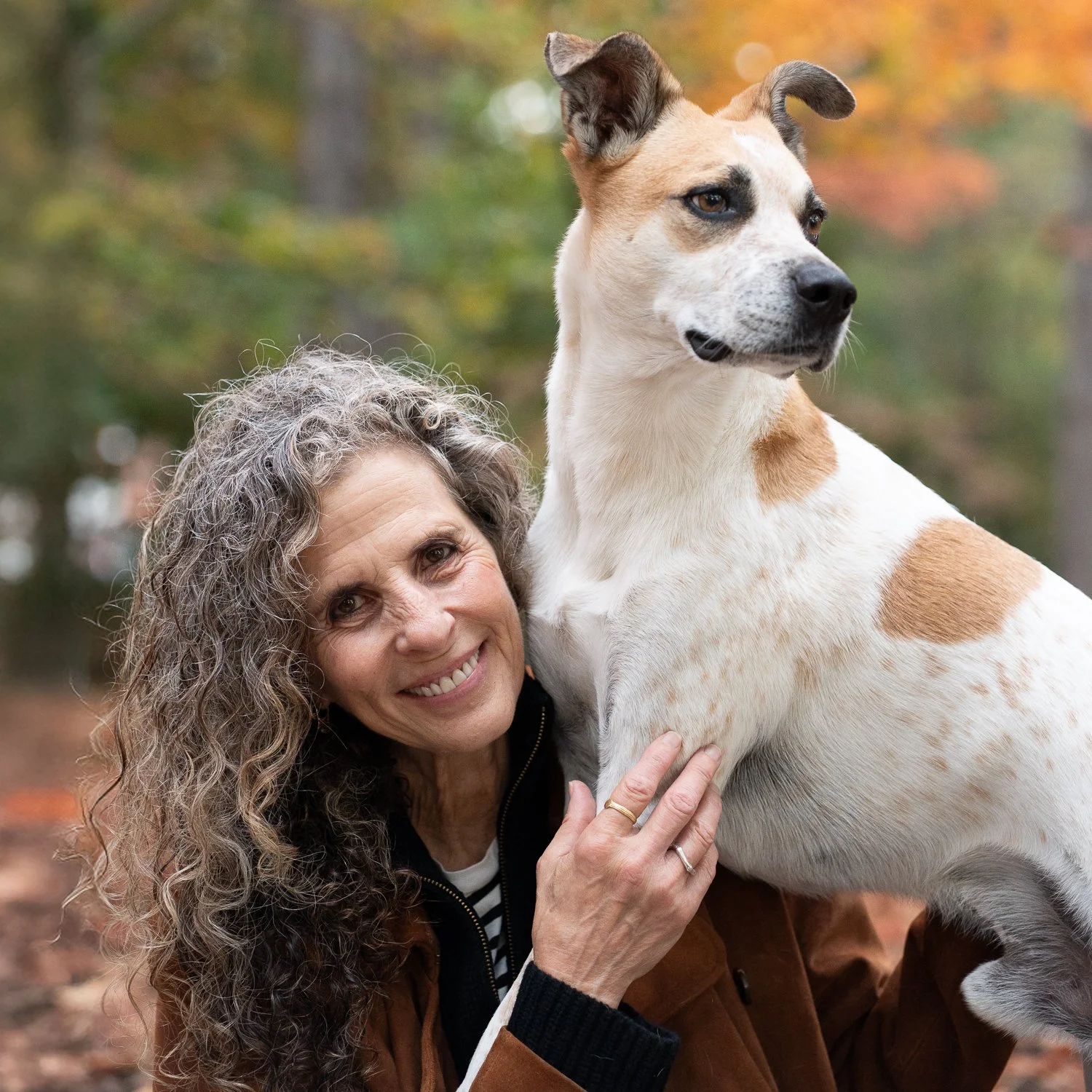 Lady sitting with her brown and white dog on her shoulder holding his arm in a Brooklyn park in fall