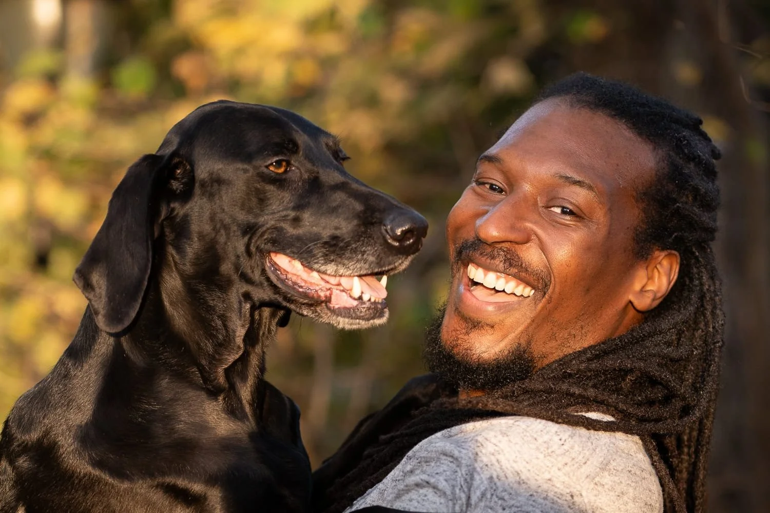 Man and black dog looking towards camera while hugging and smiling