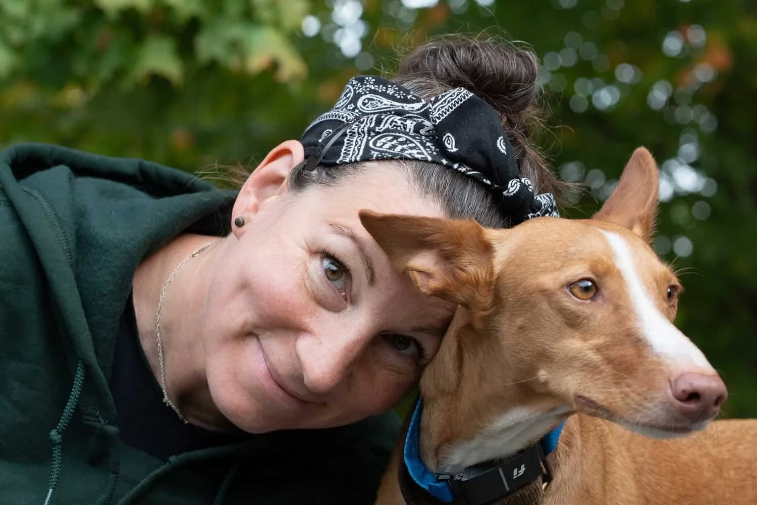 Lady smiling while resting her head on tan and white dog in a Brooklyn, NY park