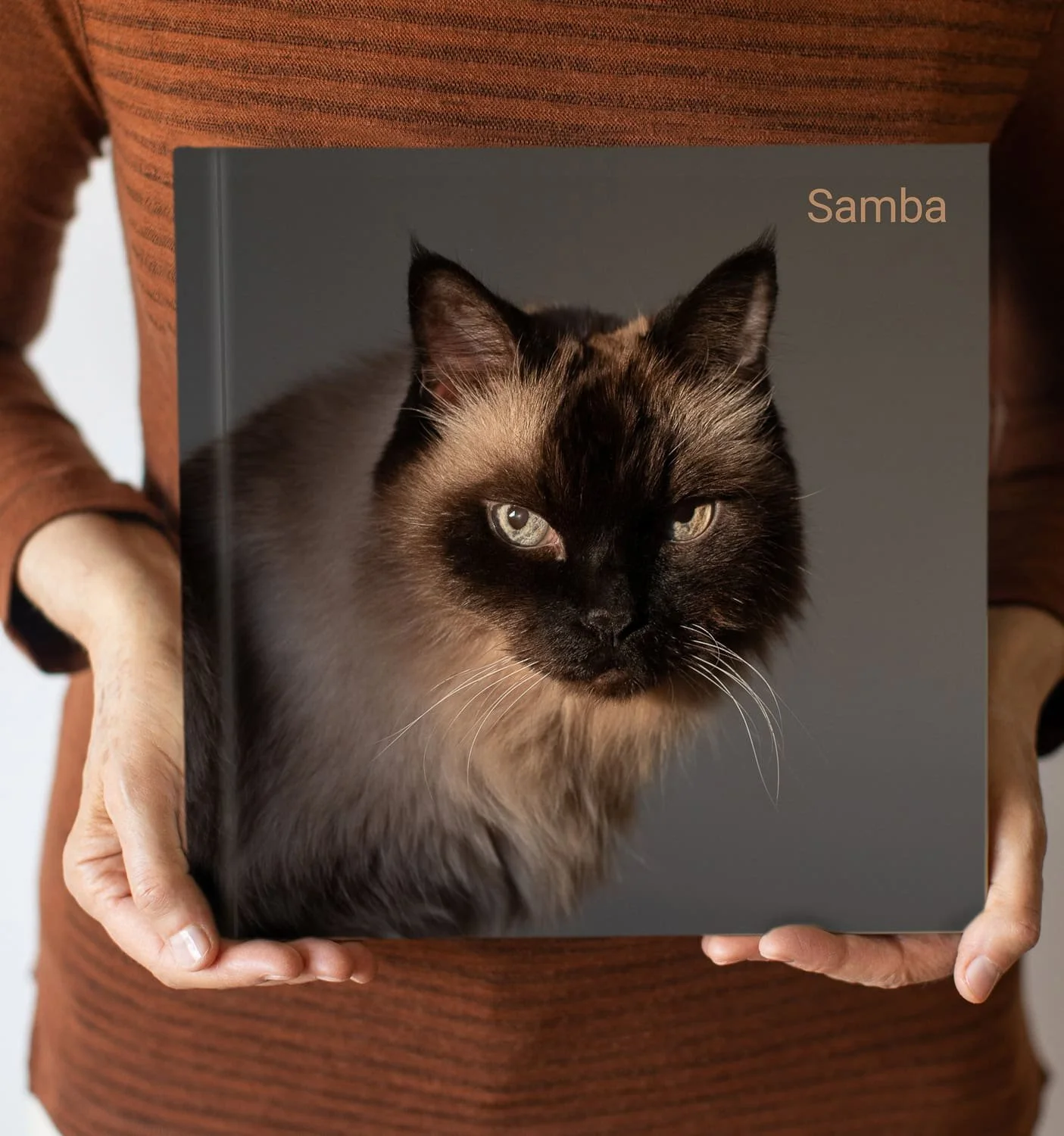 Cat on cover of custom photo book being held with hands in picture