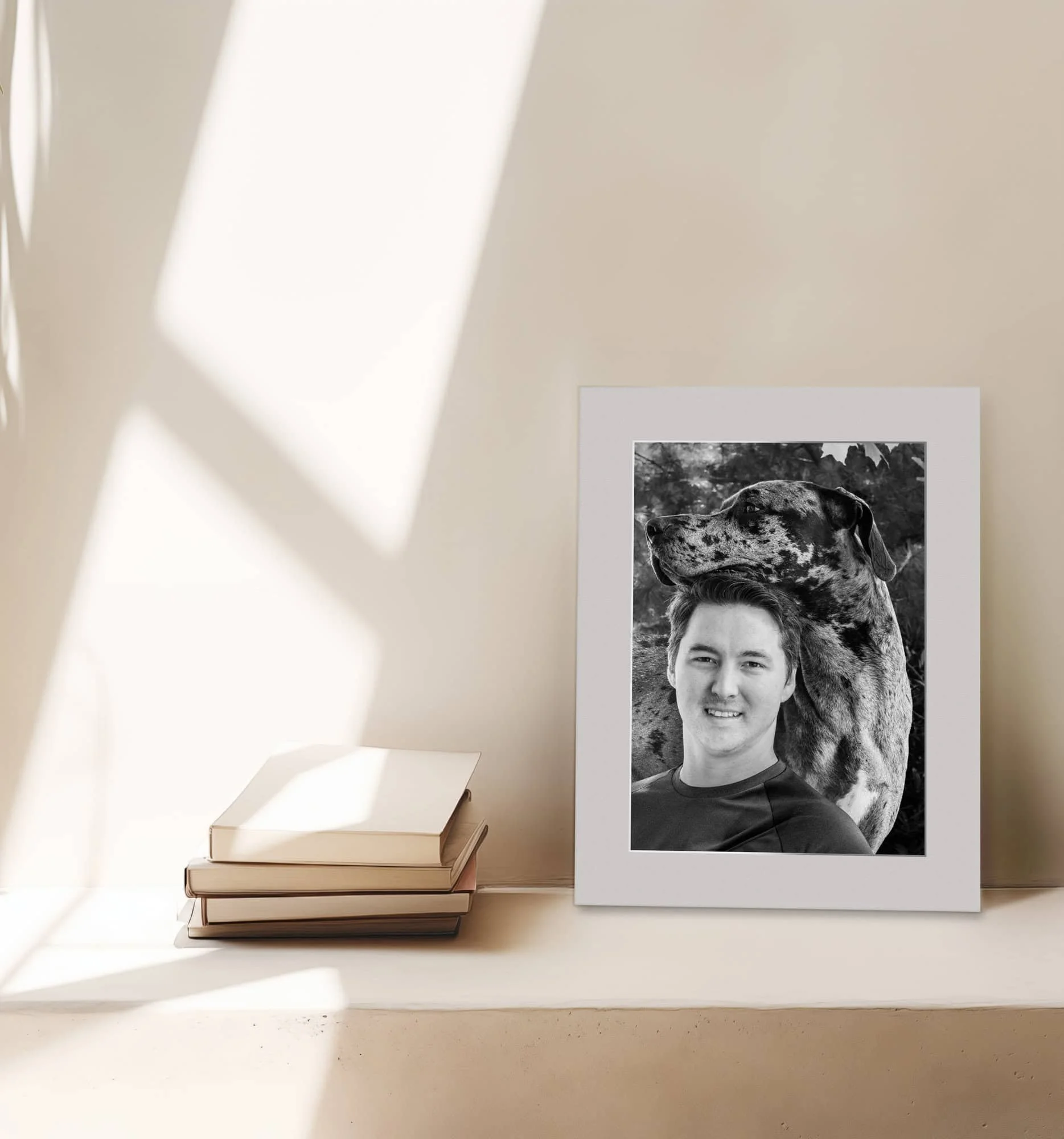 Matted photo of man and his great dane sitting on shelf next to books with light colors