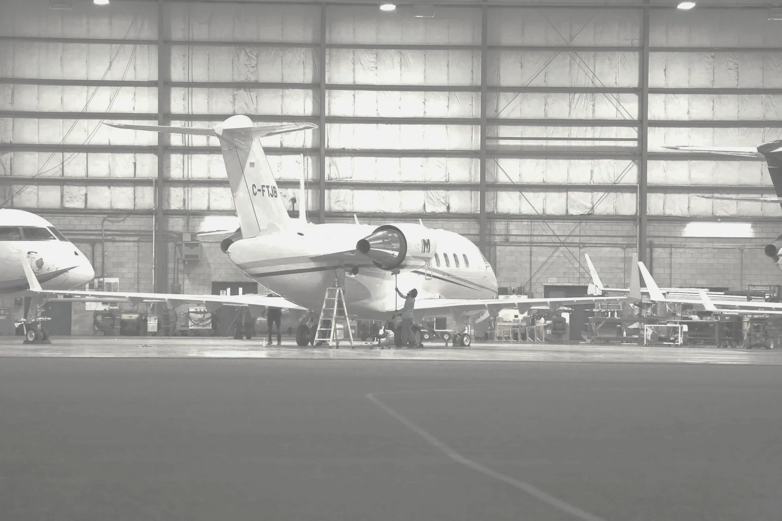 Interior of an aircraft hangar with multiple military aircraft, technicians working on one jet, and aircraft with tail numbers.