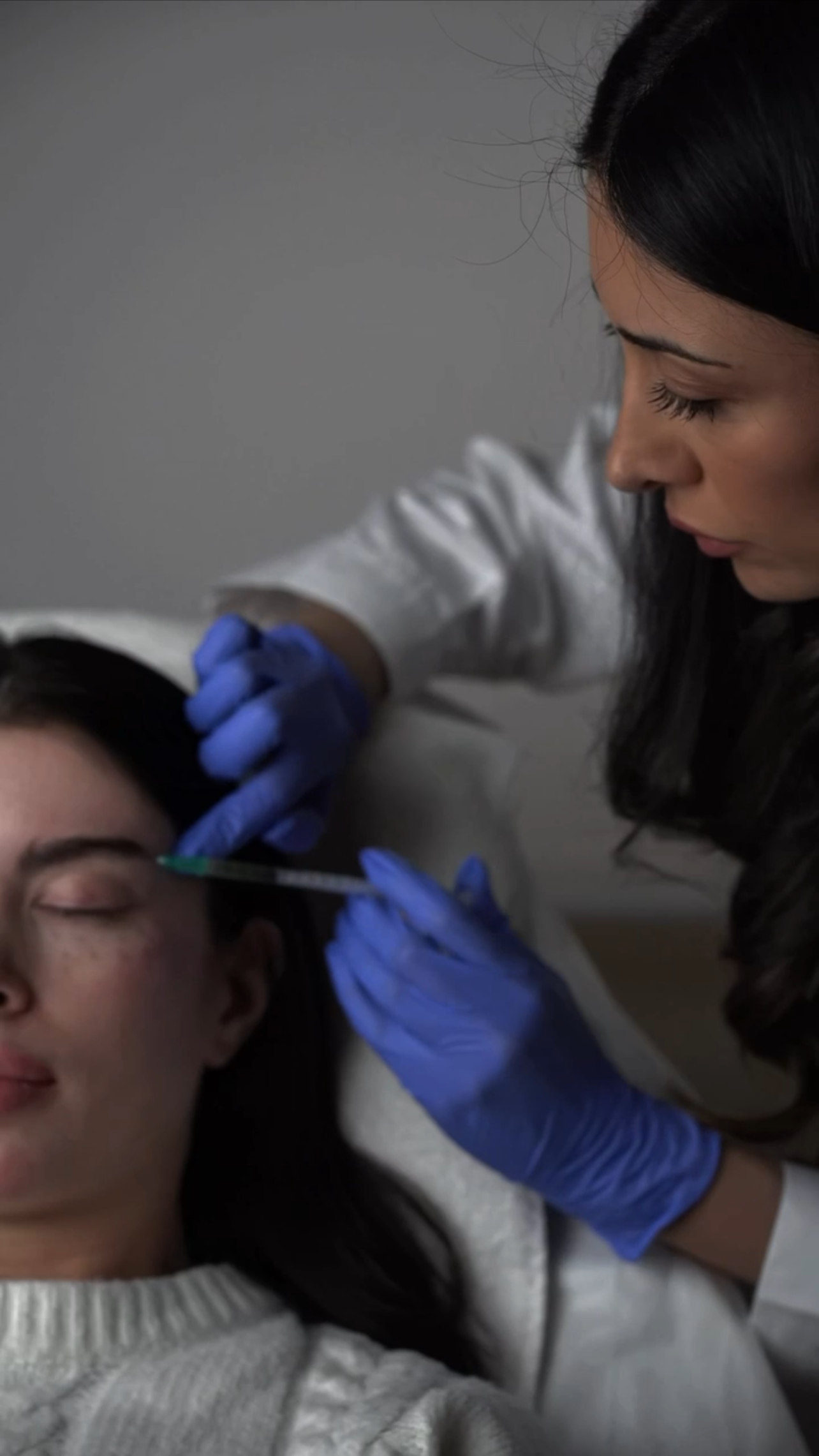 Ärztin führt einer jungen Patientin eine Injektion in den Arm durch, beide tragen blaue Handschuhe.