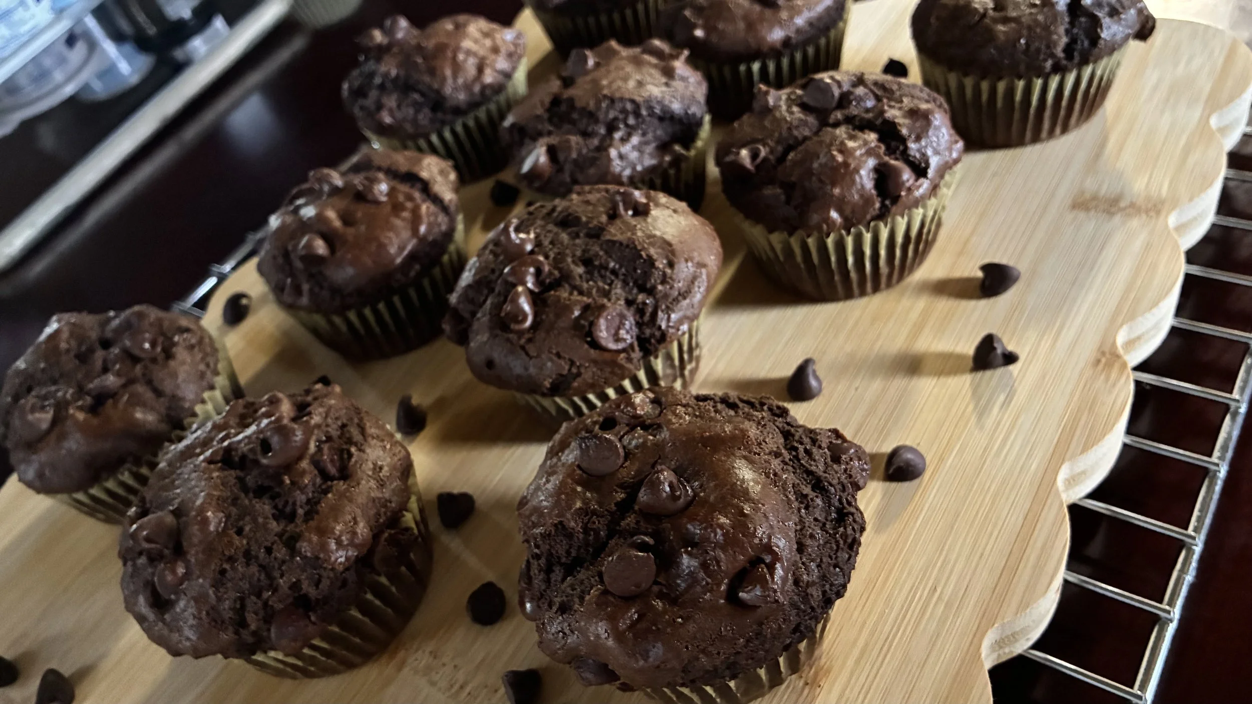 A tray of freshly baked chocolate muffins with chocolate chips on top, arranged on a wooden board.