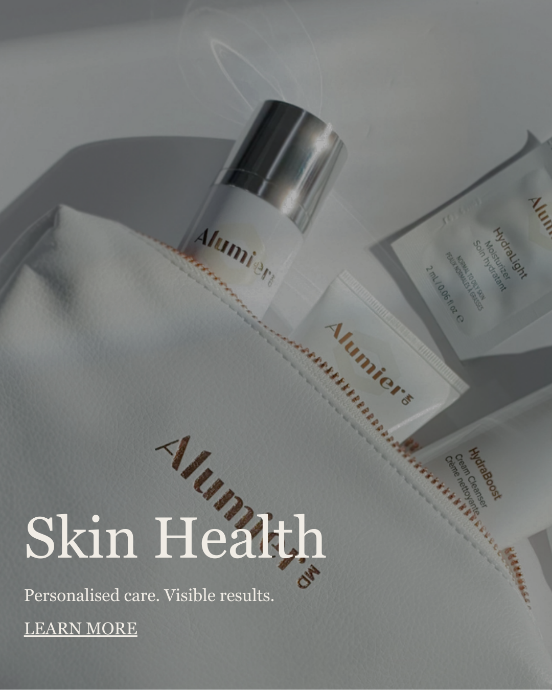 Skincare products from Alumière, including a moisturizer and a packet of HydraLight skin treatment, partially visible inside a white textured pouch with gold lettering.