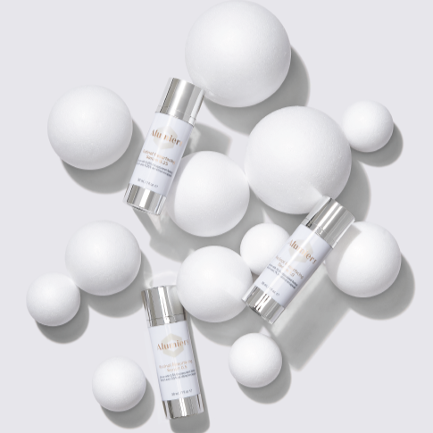 Three skincare bottles surrounded by white foam balls of various sizes on a white background.