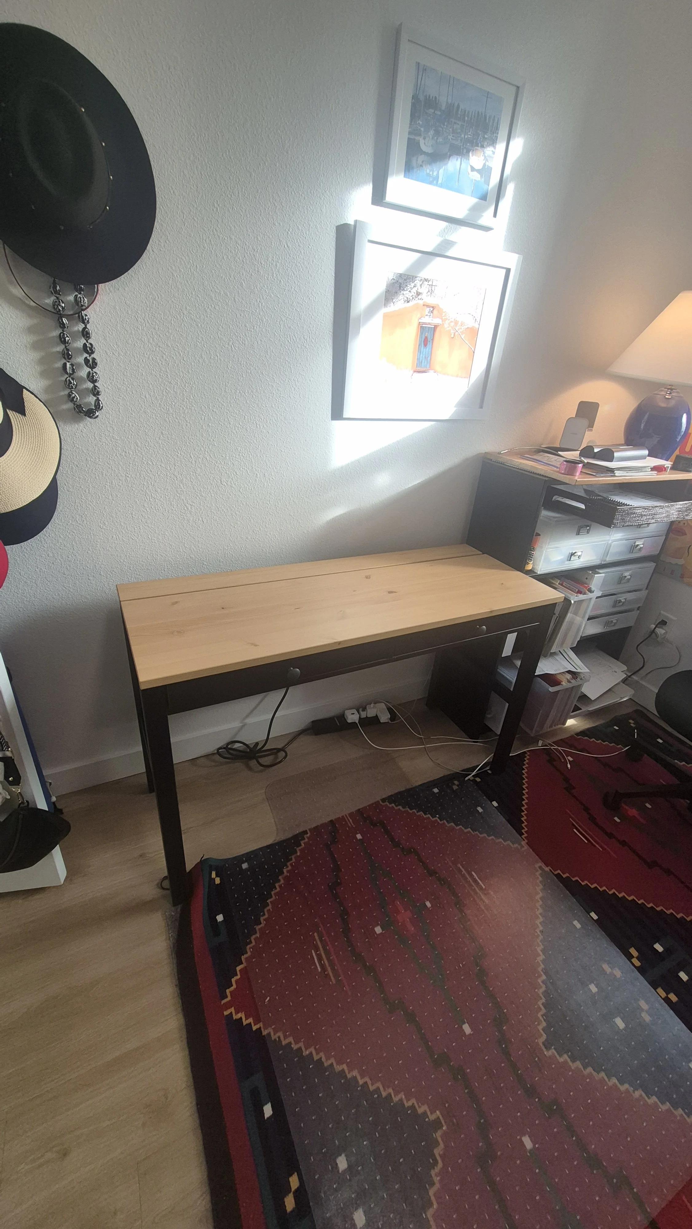 A room with a wooden desk, a black and white filing cabinet, a bedside table with a lamp, pictures on the wall, and a colorful patterned rug on the floor; Northglenn, Colorado