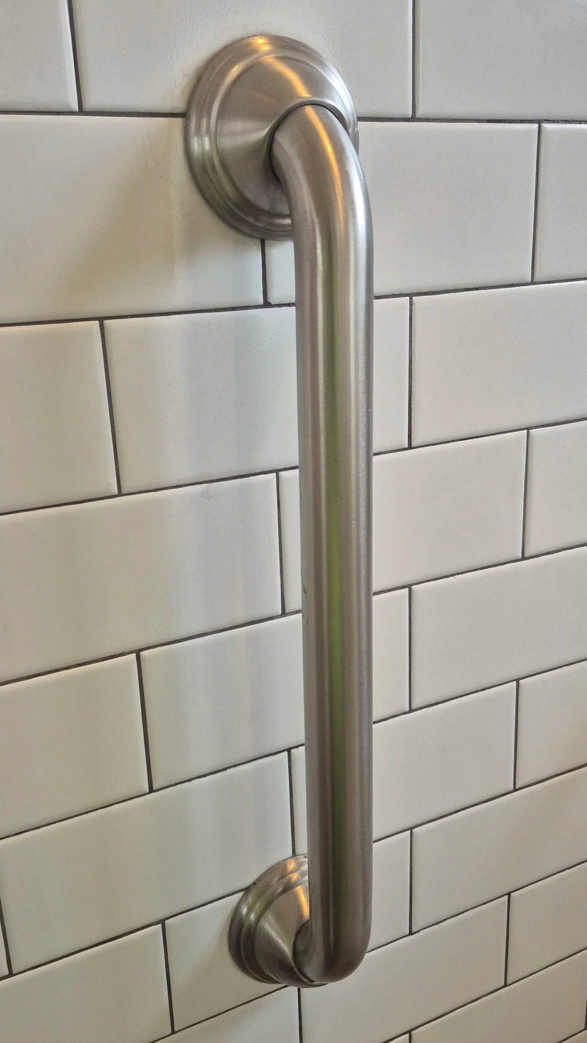Stainless steel grab bar attached to a tiled wall.